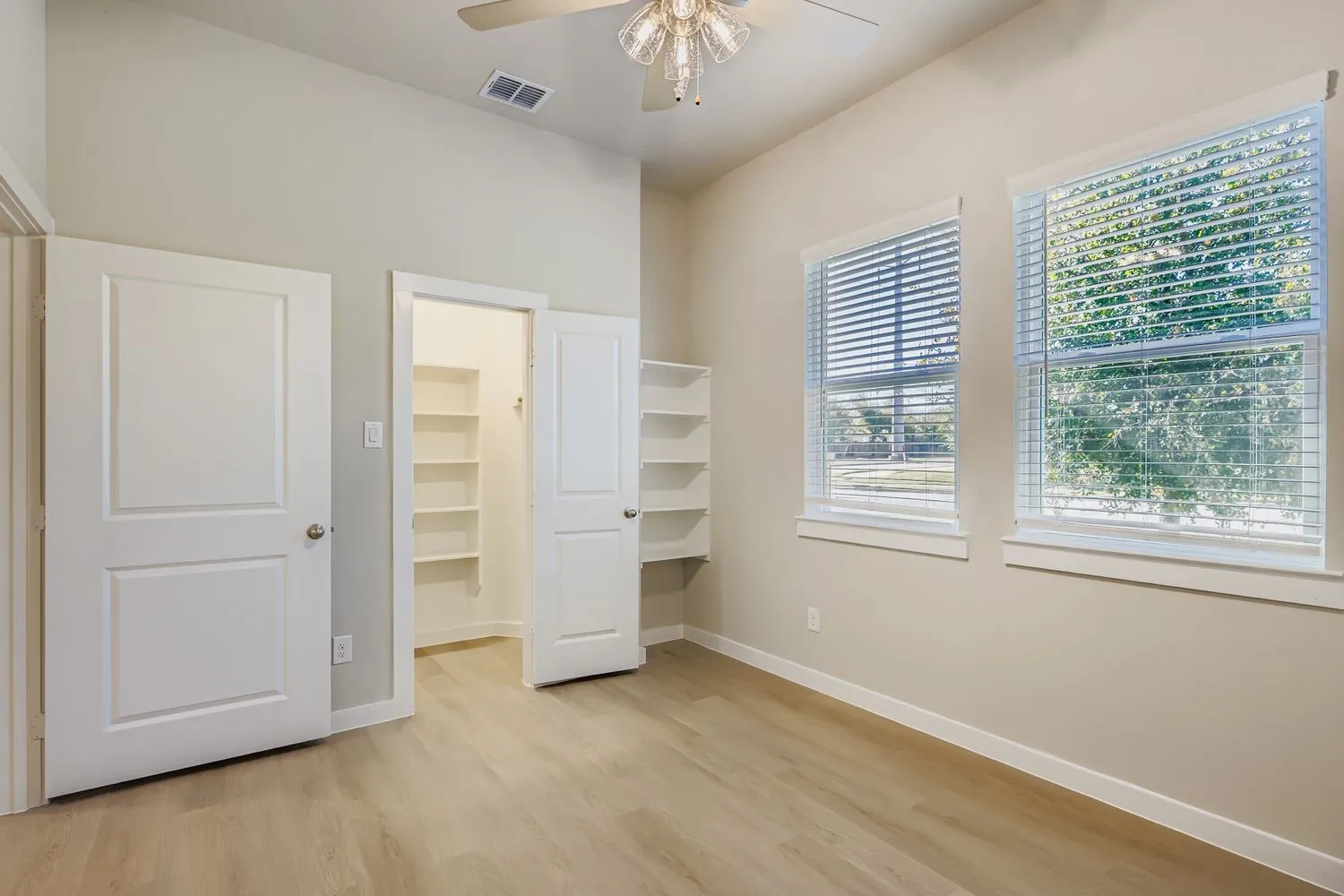 Room featuring high ceilings, wood-finish flooring, dual windows with blinds, and built-in shelving