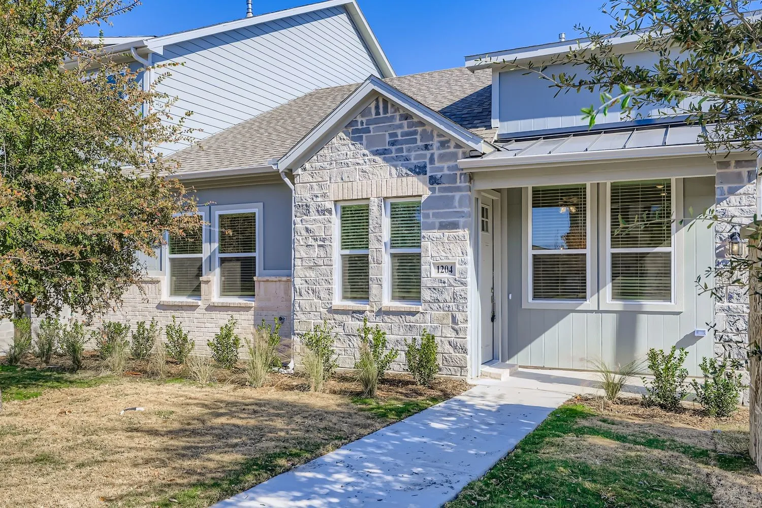 Exterior featuring stone veneer masonry, vertical panel siding, a metal roof accent over the entryway, and multi-pane windows