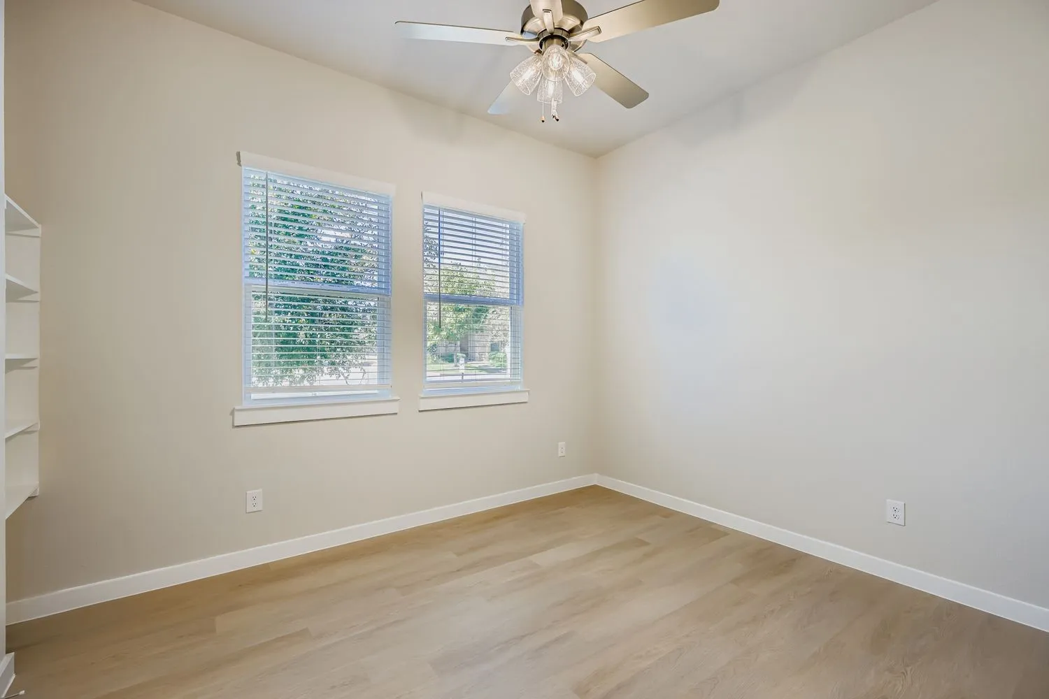 Room featuring wood-finish flooring, dual windows with blinds, built-in shelving, and a multi-light ceiling fan