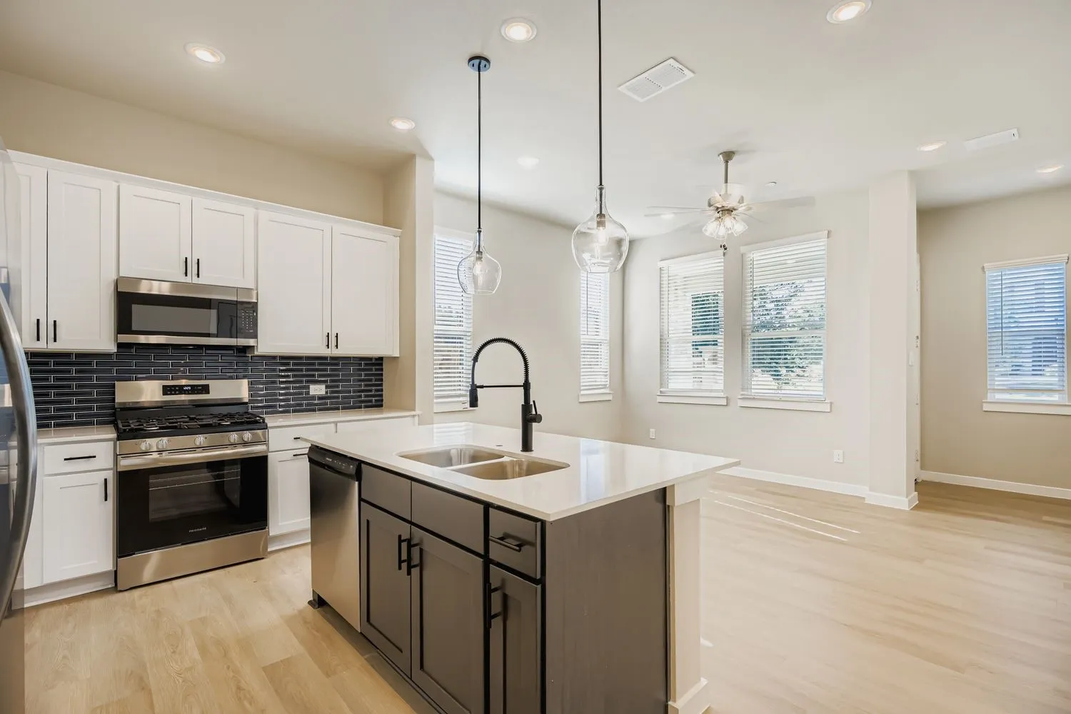 Kitchen featuring white cabinetry, a contrasting dark-toned kitchen island, stone-surface countertops, a dark-toned tile backsplash, and stainless-steel appliances