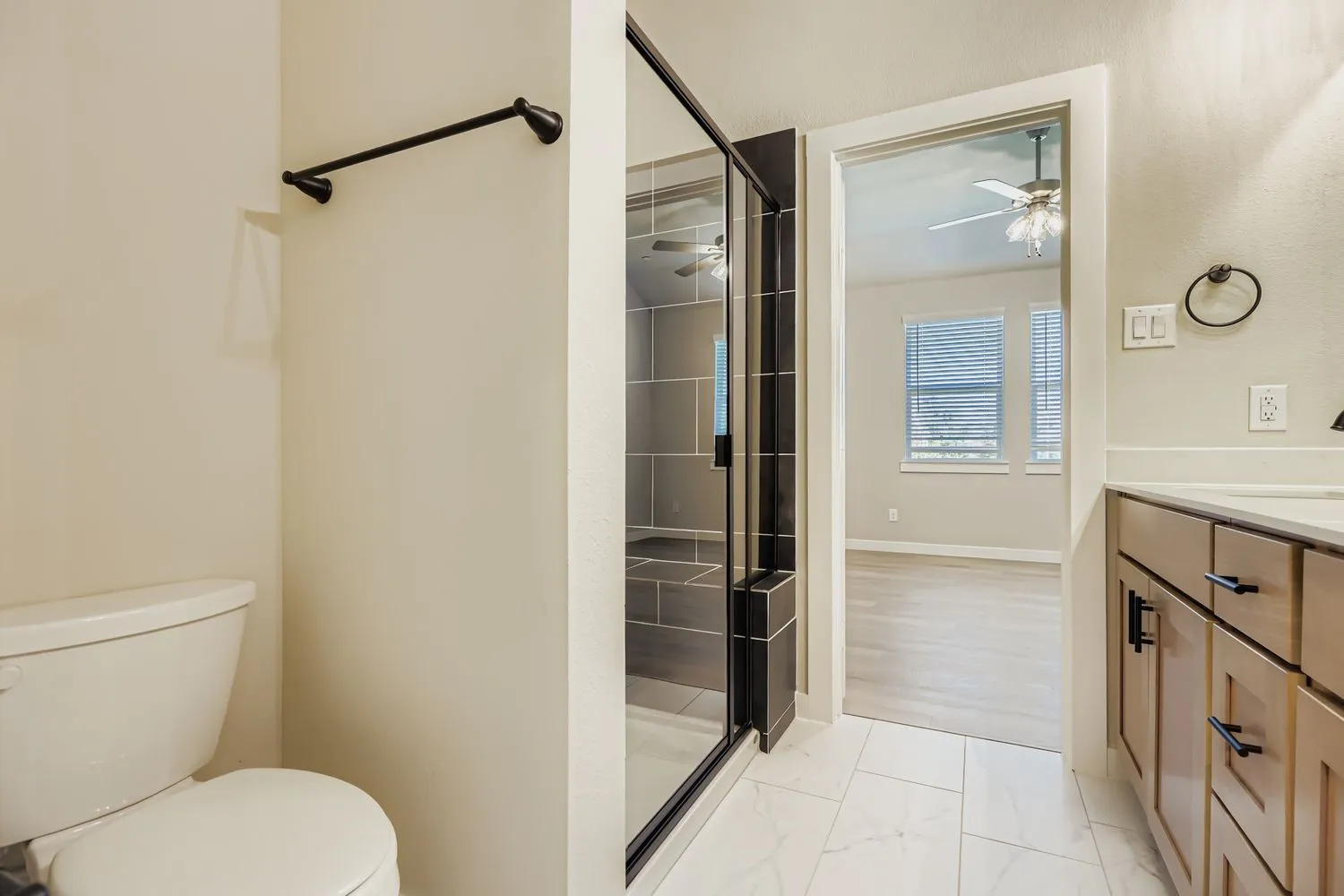 Bathroom featuring a glass-enclosed shower with large-format tile surround, light wood-tone cabinetry, matte black hardware, and stone-finish floor tiling