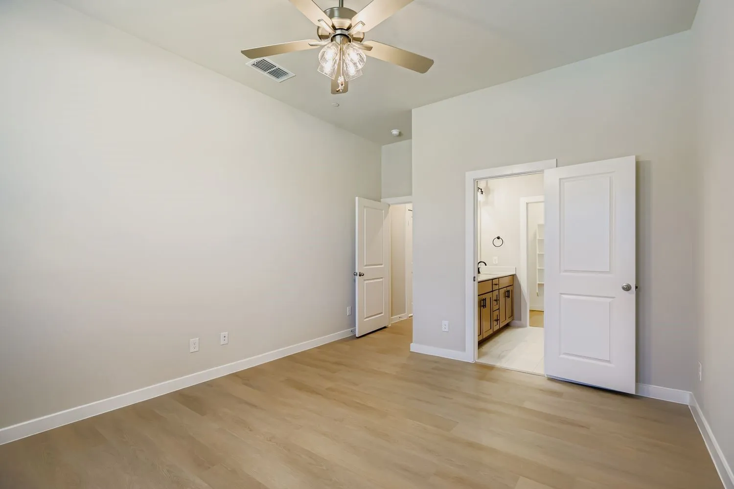 Room featuring high ceilings, wood-finish flooring, a central multi-blade ceiling fan with integrated lighting, and white interior doors