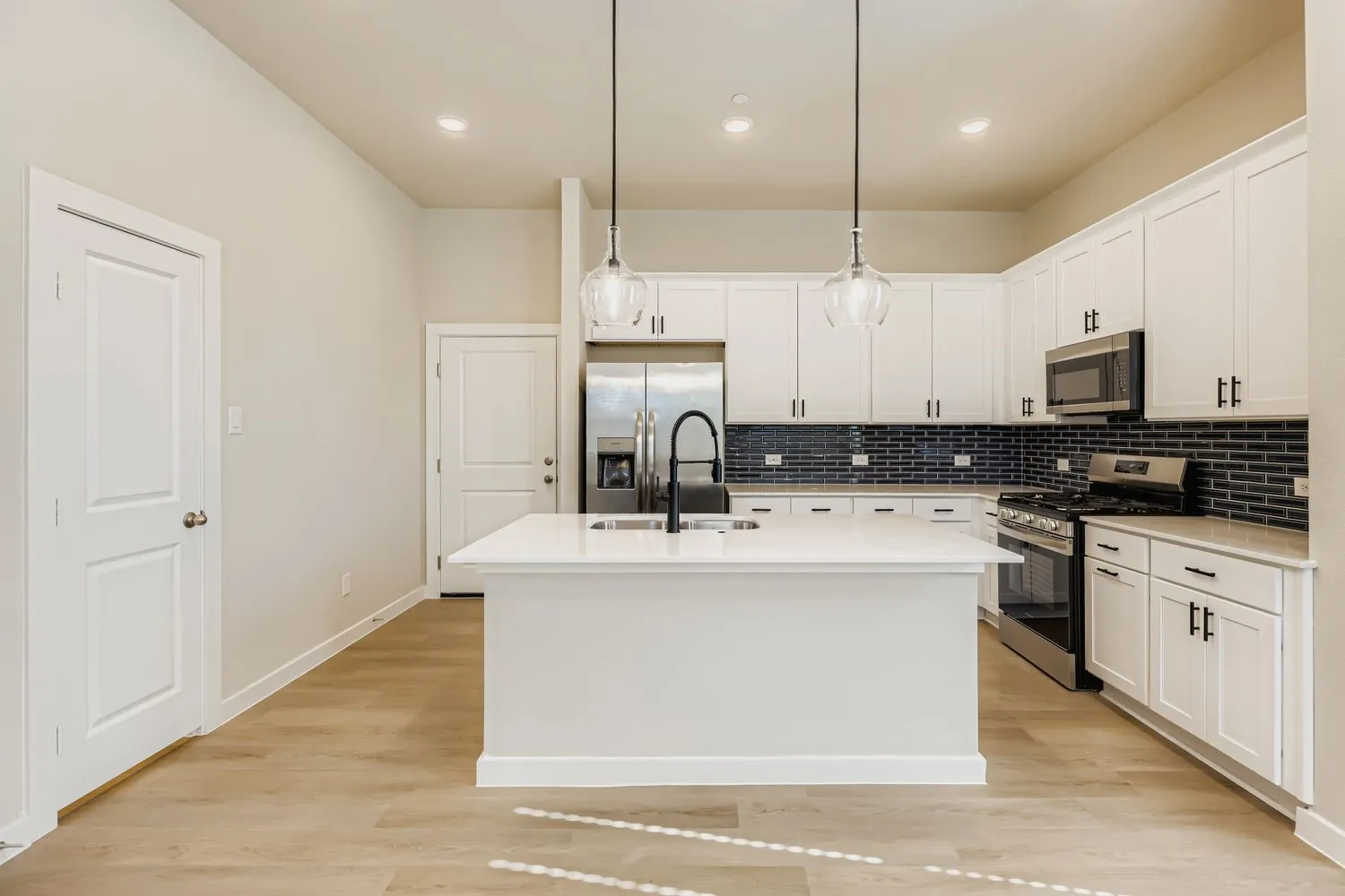 Kitchen featuring white cabinetry, quartz countertops, a central island with a high-arch faucet, dark subway tile backsplash, and wood-finish flooring