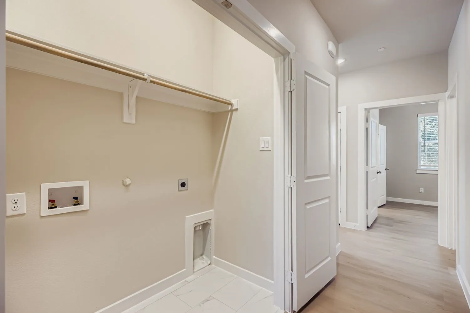 Laundry area featuring recessed water supply connections, dedicated dryer venting, overhead shelving with a hanging rod, and light-toned tile flooring