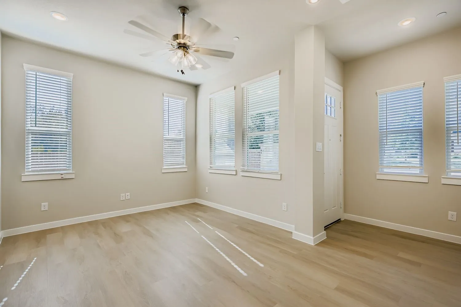 Neutral-toned interior featuring wood-finish flooring, recessed lighting, a brushed-nickel ceiling fan, and multiple windows with horizontal blinds