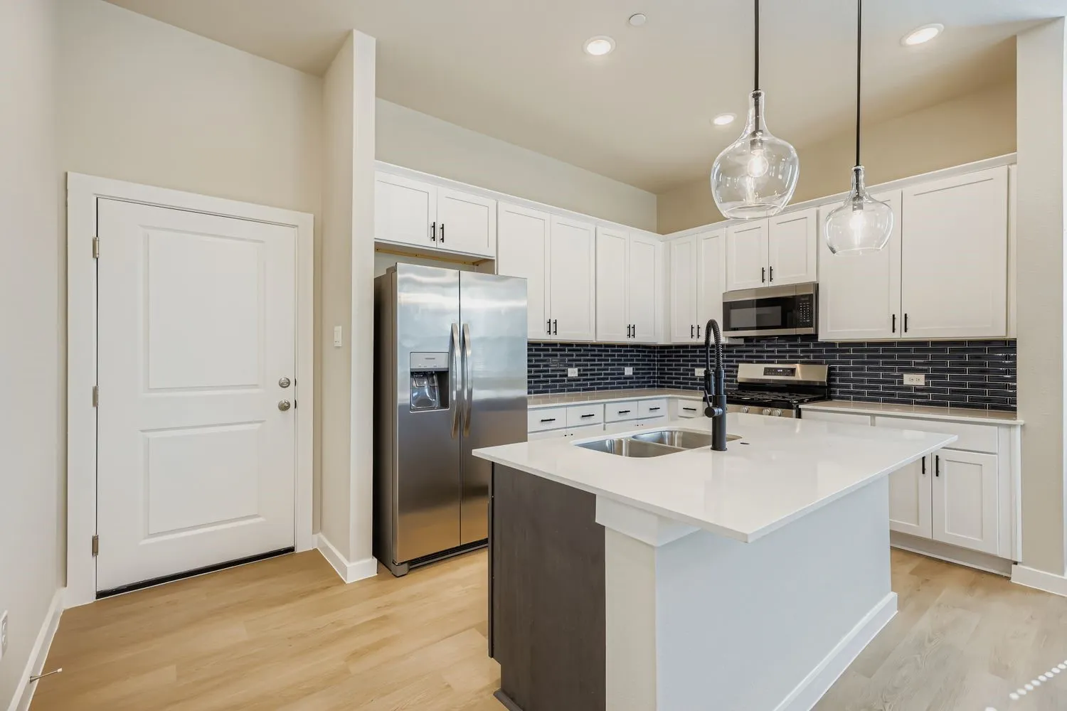 Kitchen featuring white cabinetry, a center island with a stone-finish countertop, dark subway tile backsplash, stainless steel appliances, and pendant lighting