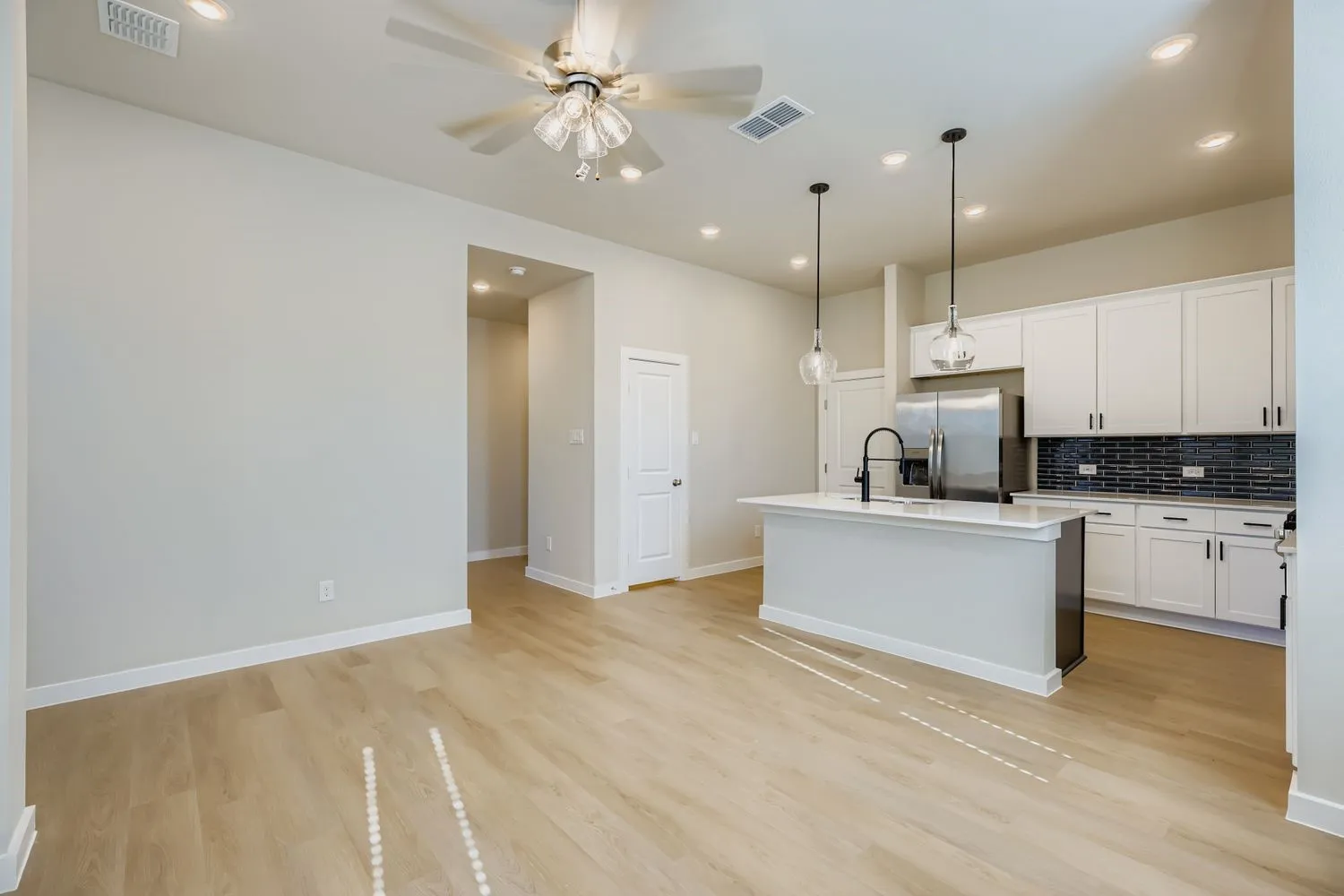 Kitchen featuring white shaker-style cabinetry, quartz countertops, a black tile backsplash, stainless steel appliances, and wood-finish flooring