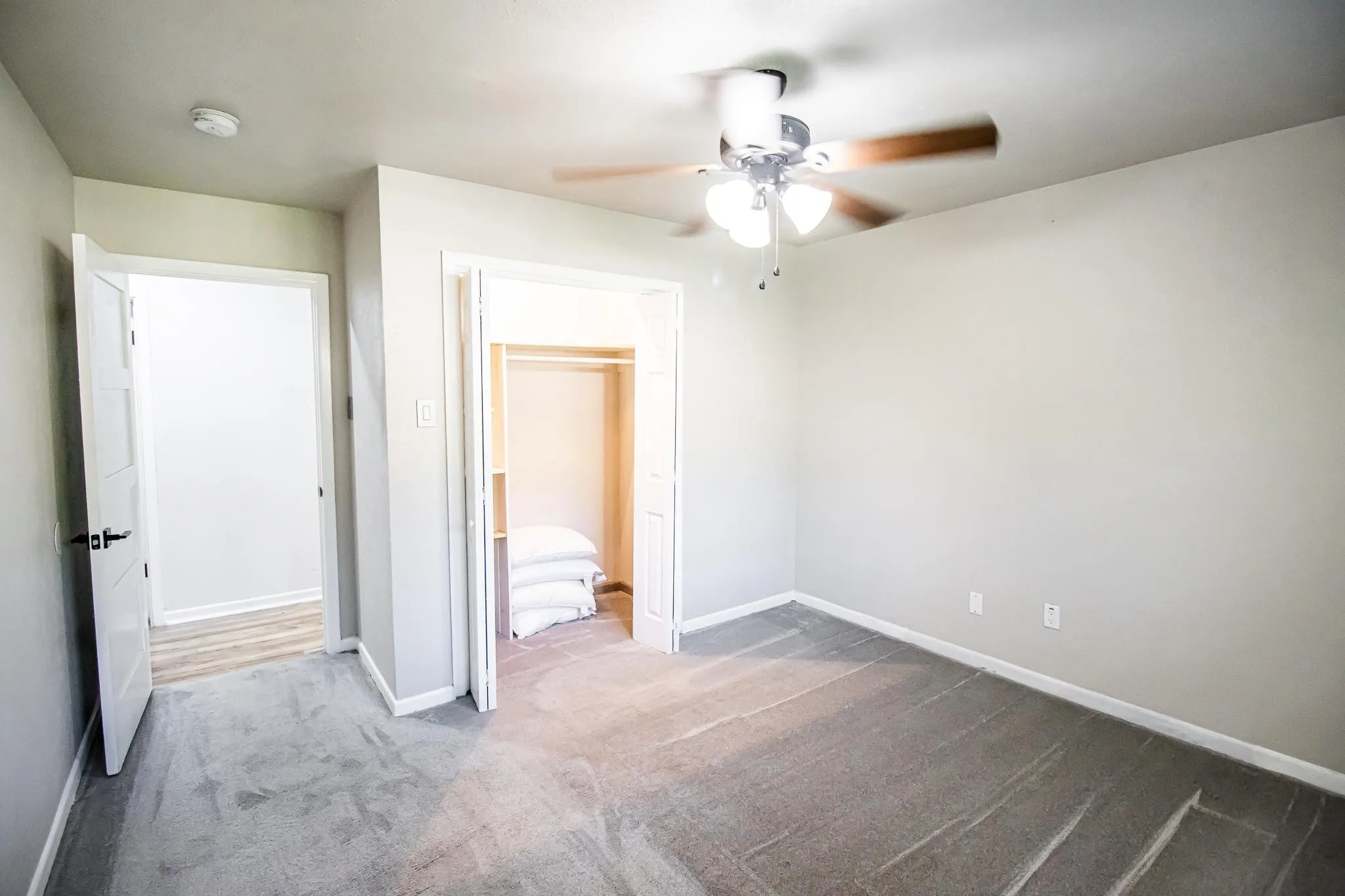 Neutral-toned interior featuring wall-to-wall carpeting, bi-fold closet doors, a multi-blade ceiling fan with integrated lighting, and white interior doors with matte black hardware