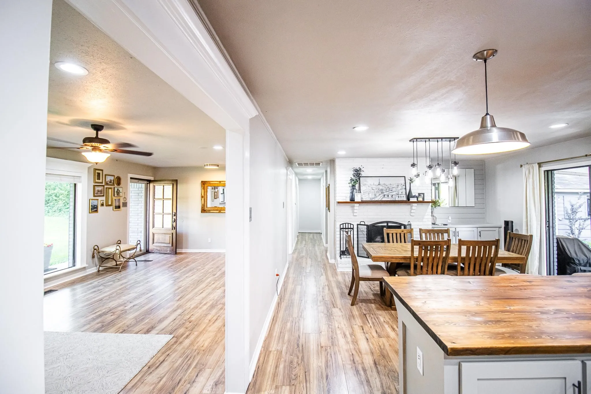 Wood-finish flooring, recessed lighting, wood-topped kitchen island, painted brick fireplace, and pendant light fixtures