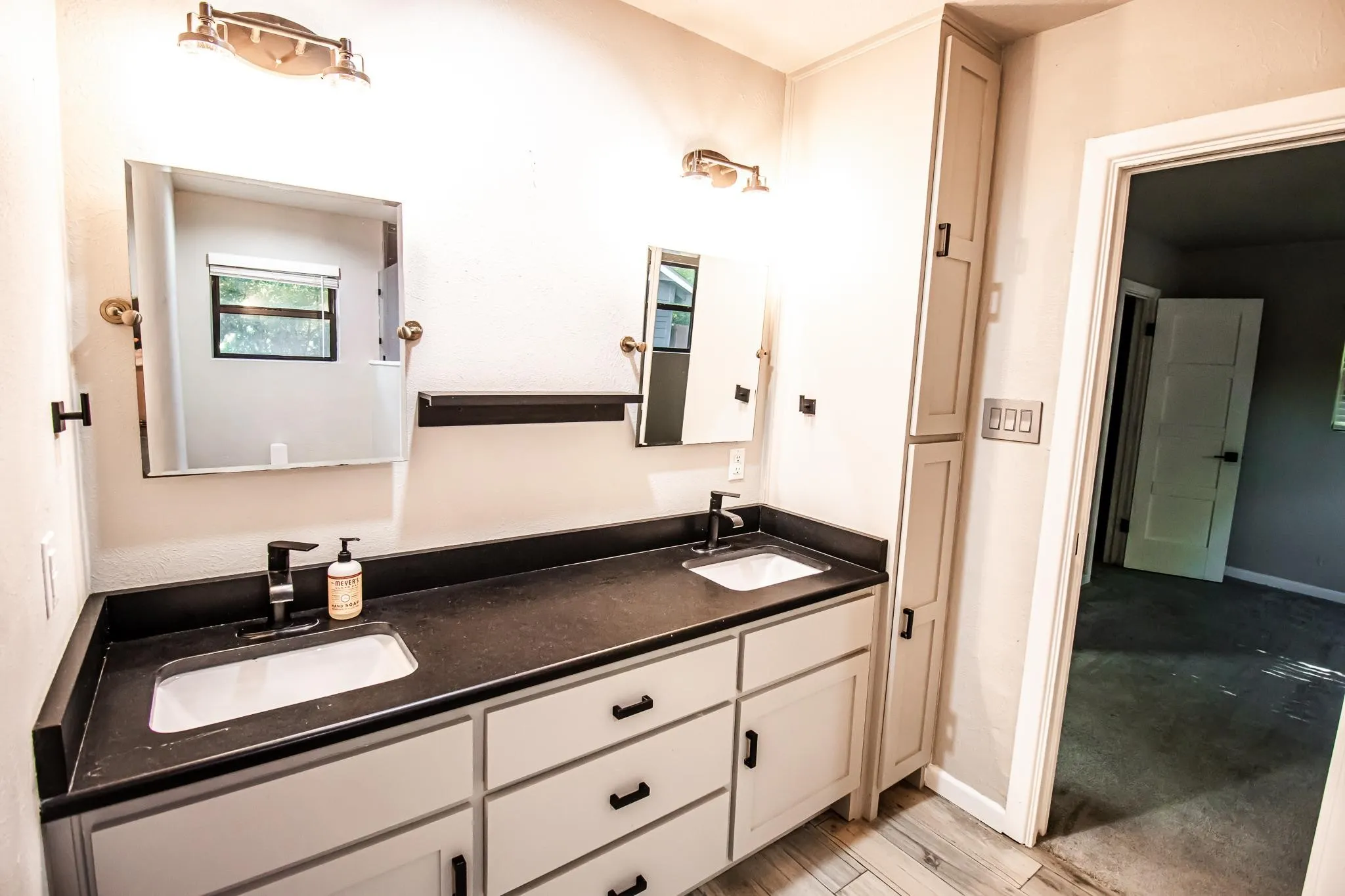 Dual-sink vanity featuring a dark countertop, white shaker-style cabinetry, matte black hardware, and integrated floor-to-ceiling cabinetry