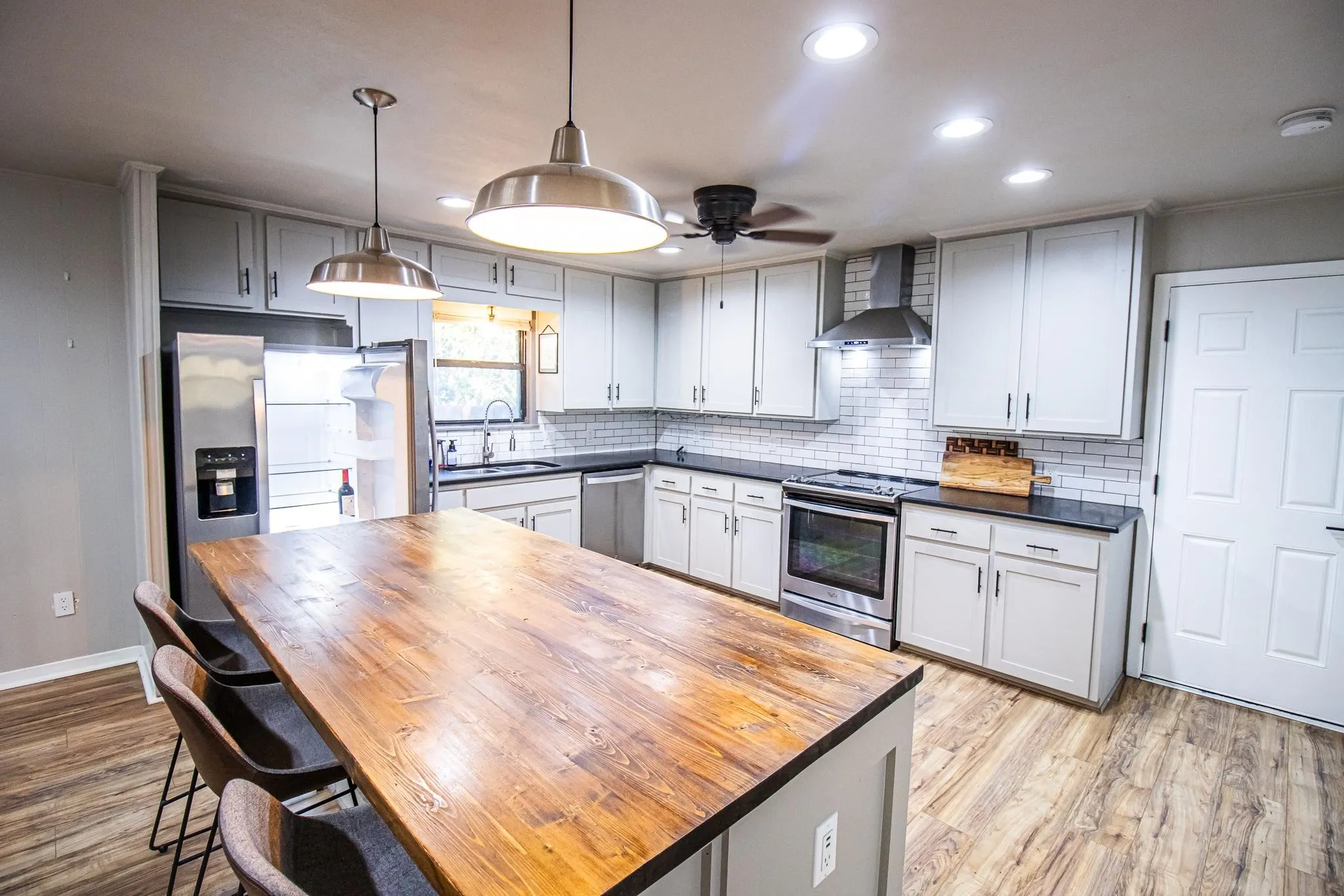 Kitchen featuring a central island with a butcher block countertop, white shaker-style cabinetry, stainless steel appliances, subway tile backsplash, and wood-finish flooring