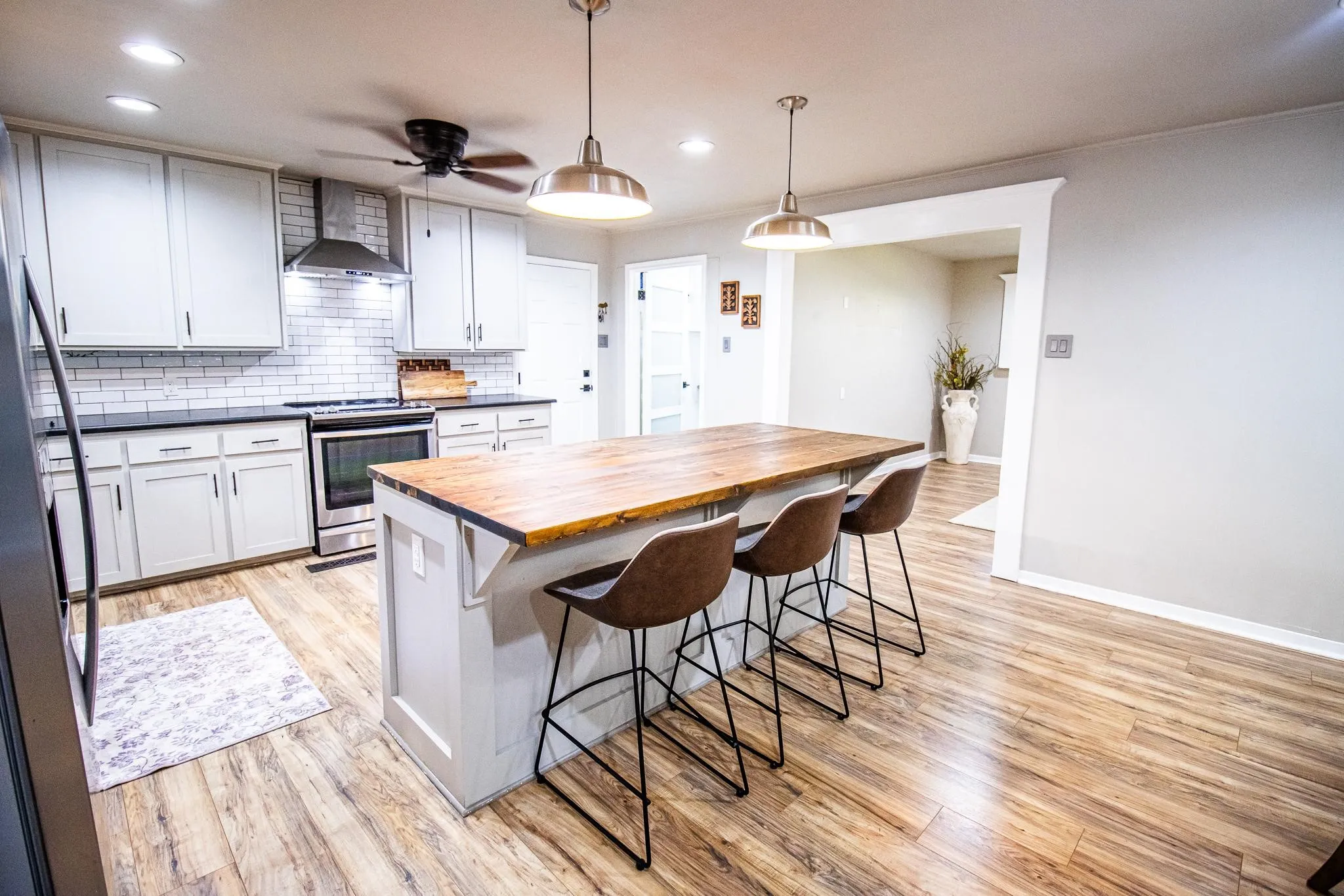Kitchen featuring a center island with a wood-finish countertop, white cabinetry, subway tile backsplash, wood-finish flooring, and pendant lighting