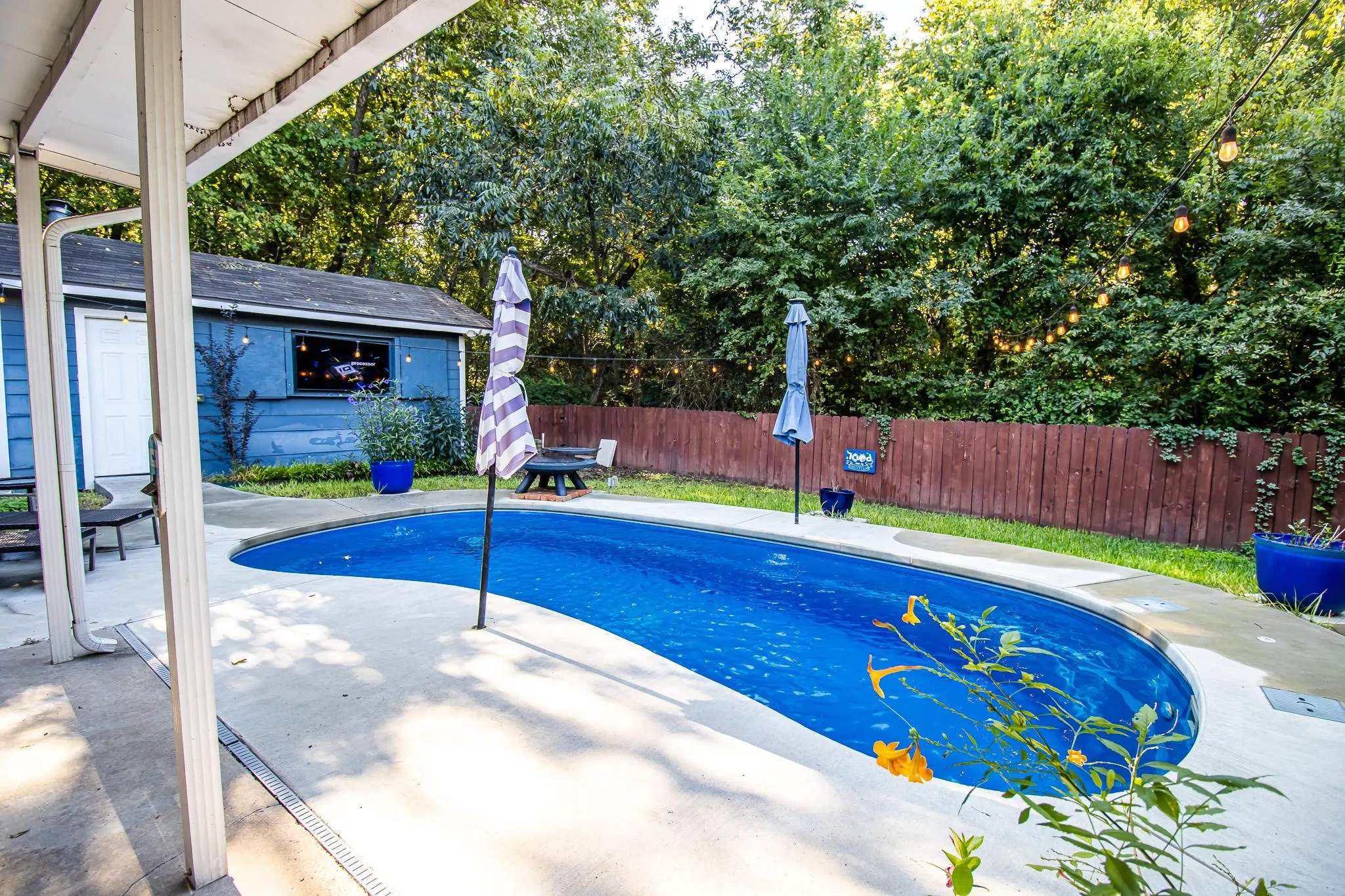 Curved in-ground swimming pool featuring a concrete deck and wood-style privacy fencing surrounded by mature trees