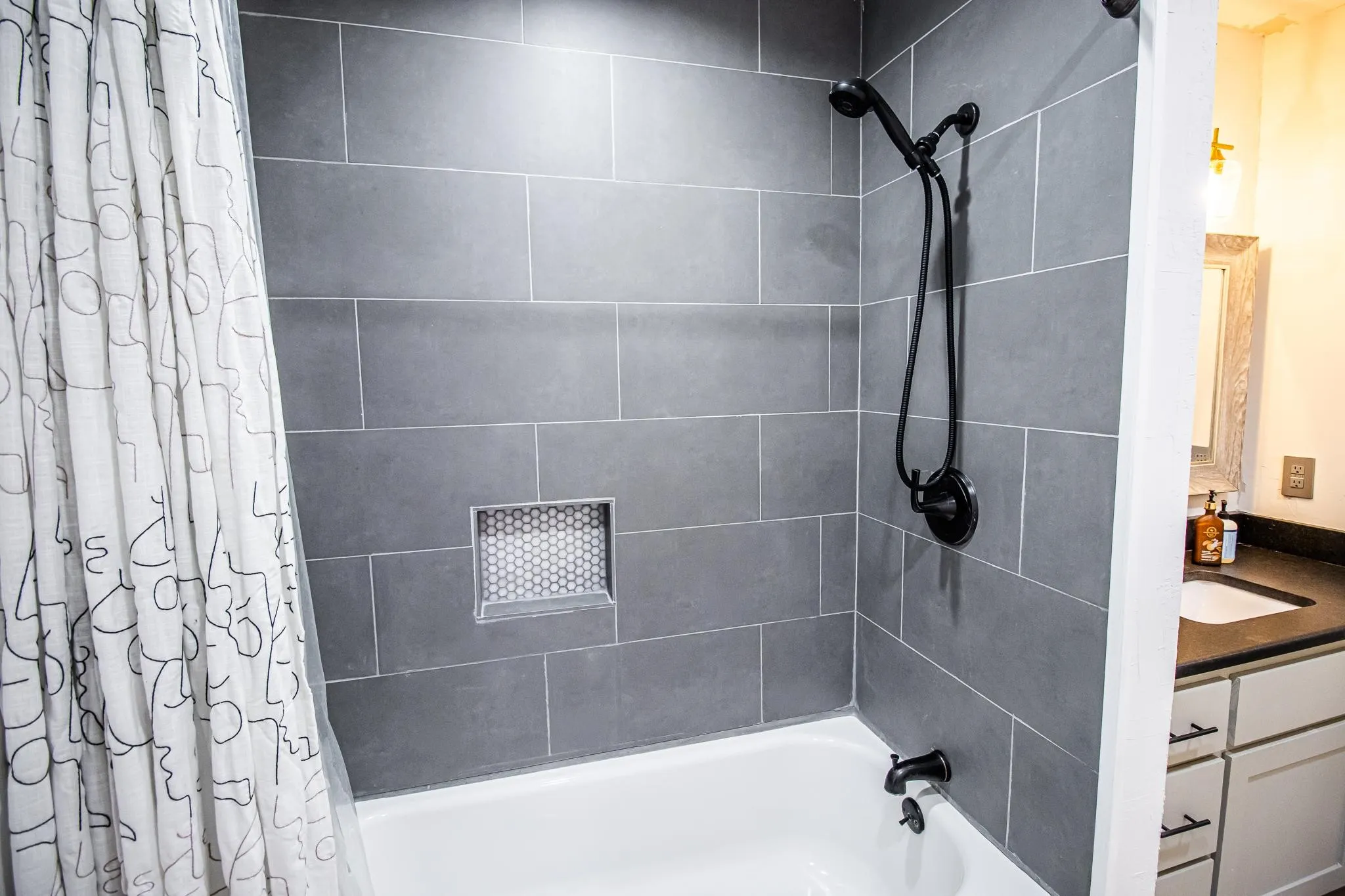 Shower area featuring large-format dark gray wall tile, a recessed hexagonal tile niche, and matte black plumbing fixtures