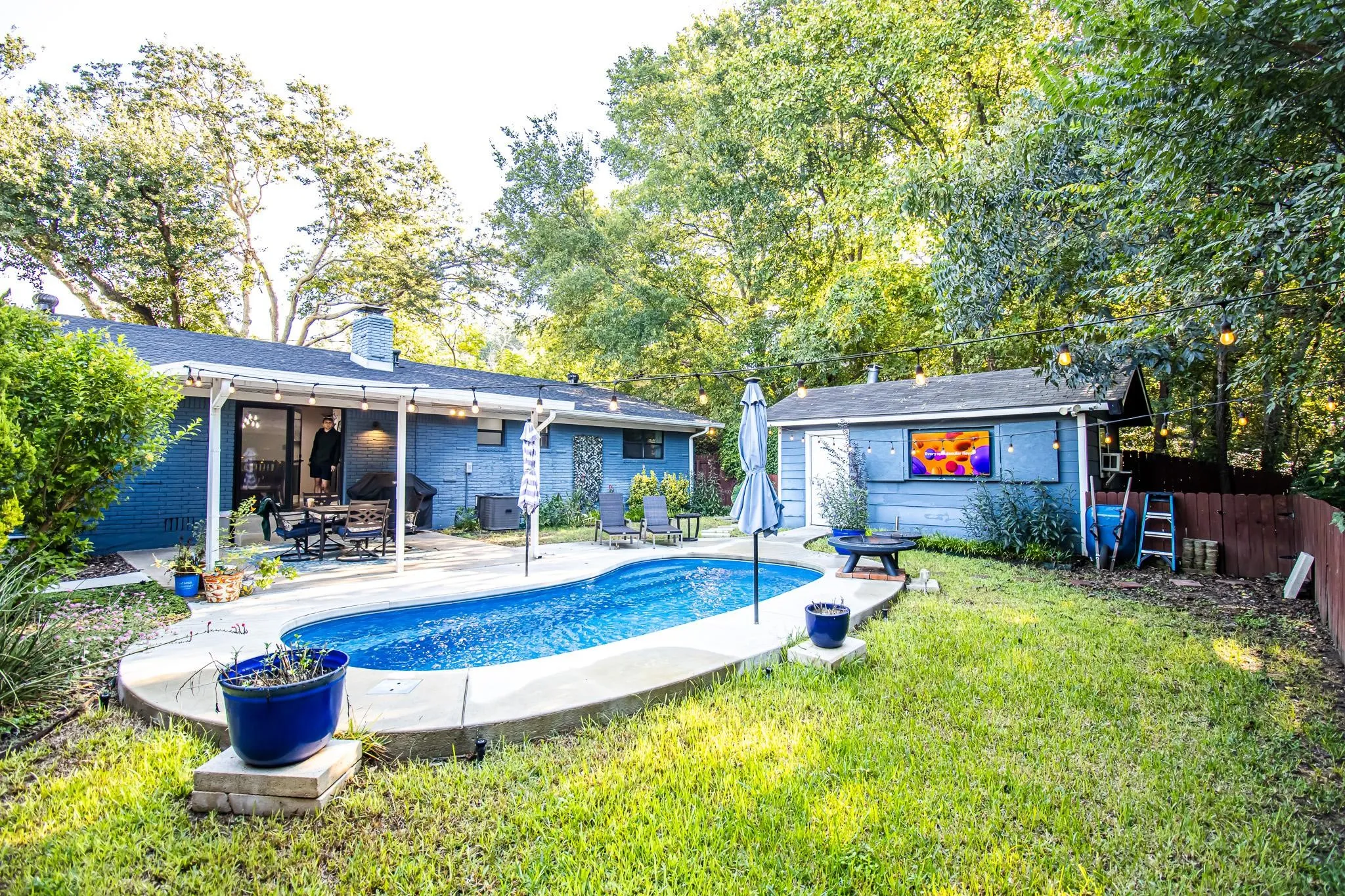 Expansive backyard featuring an in-ground pool with concrete decking, covered patio, detached structure, and mature tree canopy