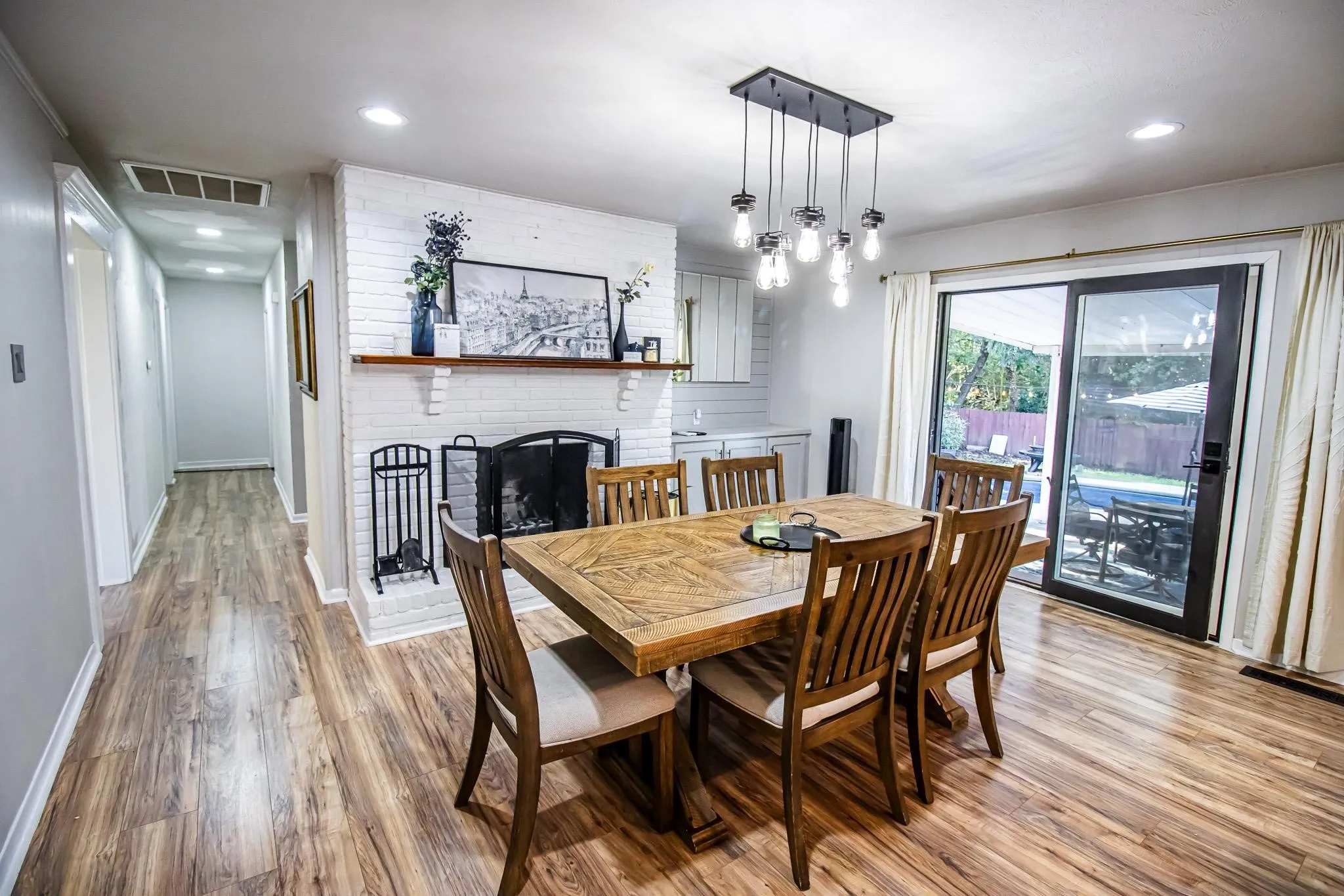 Dining area featuring wood-finish flooring, a painted brick fireplace with a wood mantel, a multi-pendant industrial-style light fixture, built-in cabinetry, and sliding glass doors