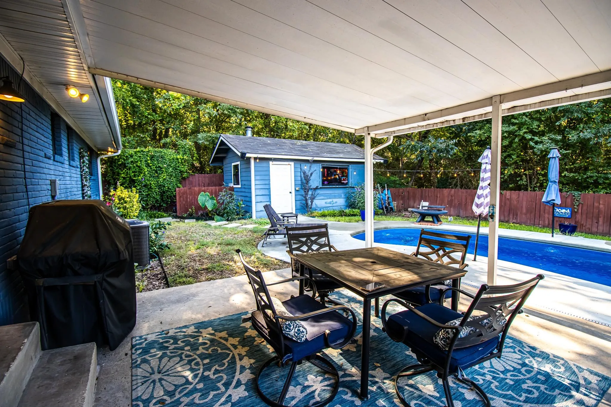 Covered concrete patio, in-ground swimming pool, detached workshop, and wood-panel fencing