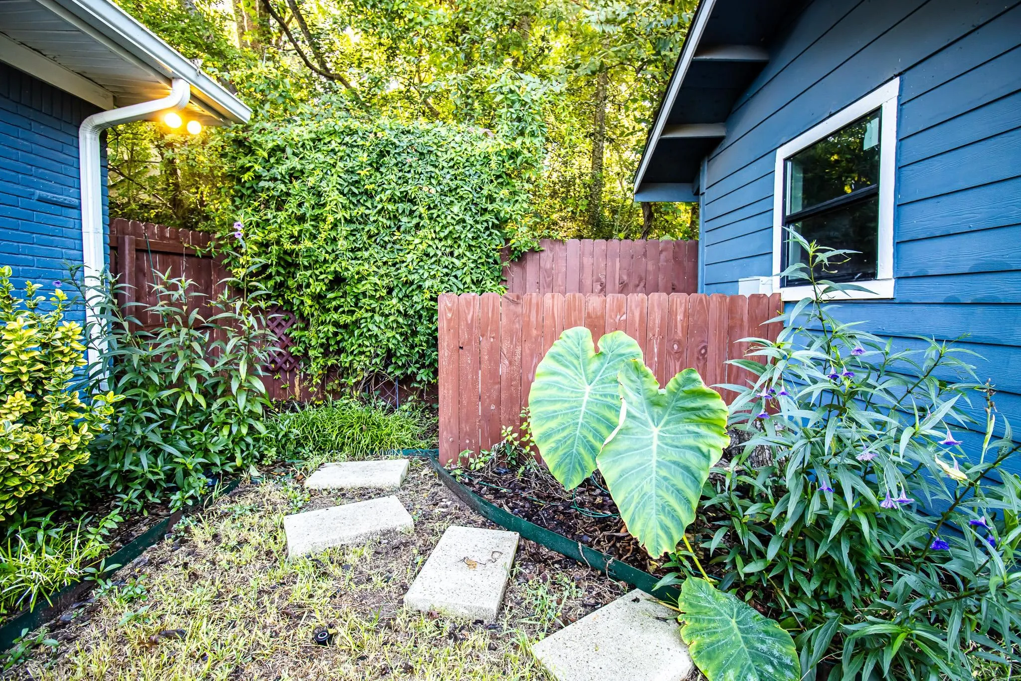 Exterior space featuring horizontal lap siding, wood privacy fencing, a concrete paver walkway, and established landscaping