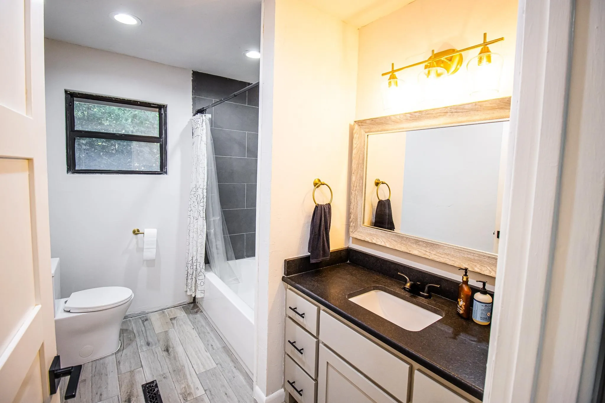 Bathroom featuring a vanity with dark solid-surface countertop, rectangular undermount sink, wood-finish flooring, recessed lighting, and a bathtub with dark tile surround