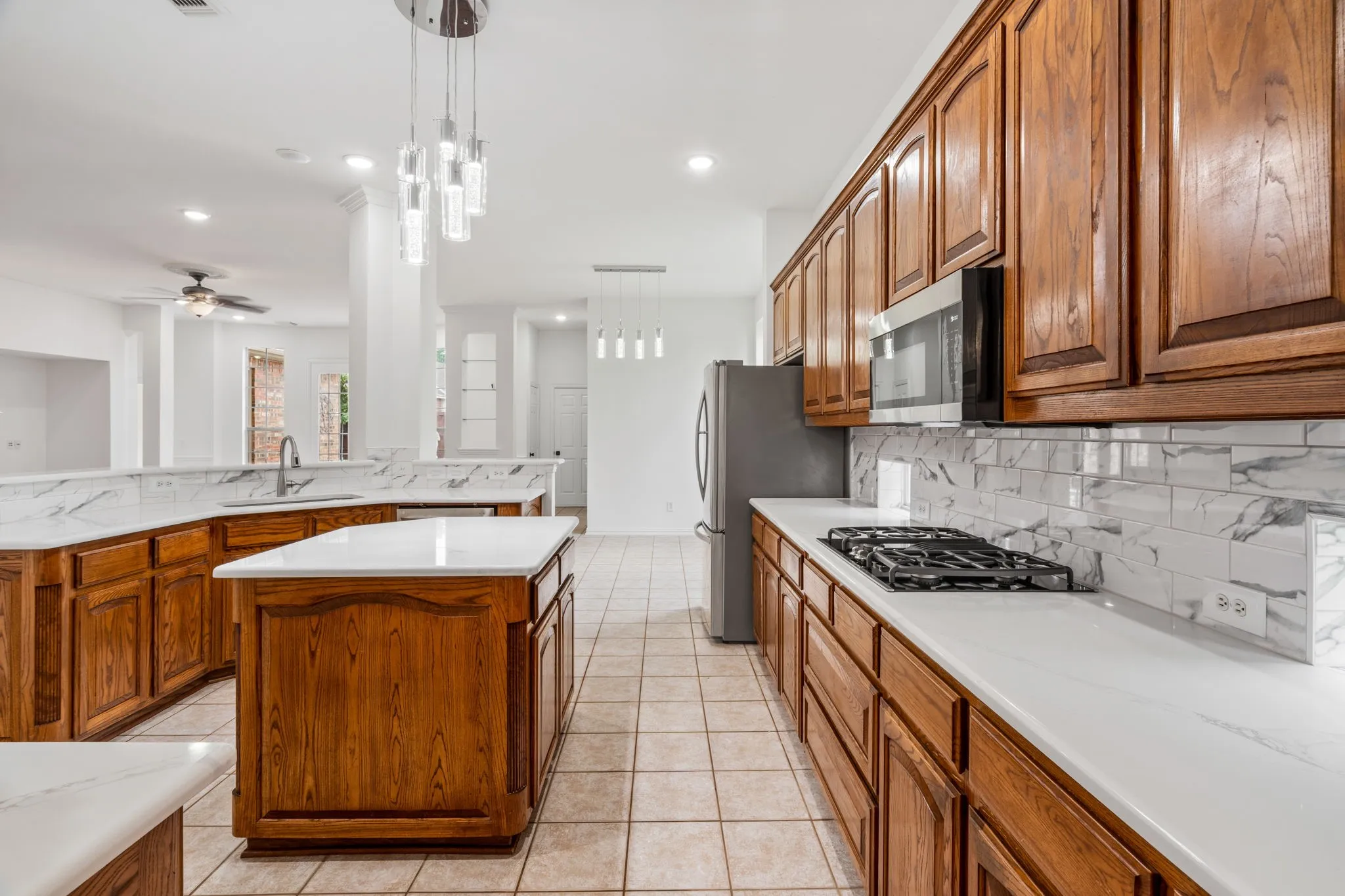 Spacious kitchen featuring an island, gas cooktop, built-in microwave, wood cabinetry, and tile flooring