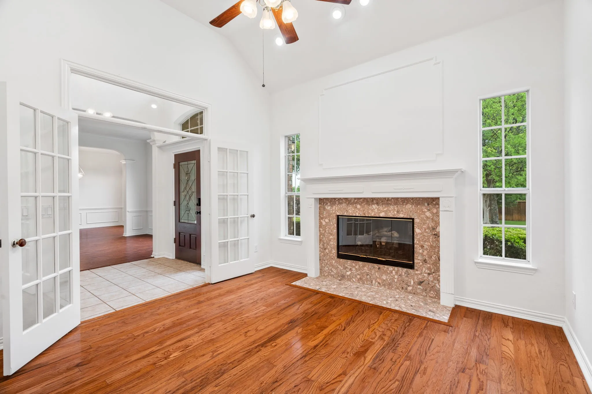 Vaulted ceiling with a ceiling fan, fireplace with a tile surround and hearth, wood-finish flooring, and French doors