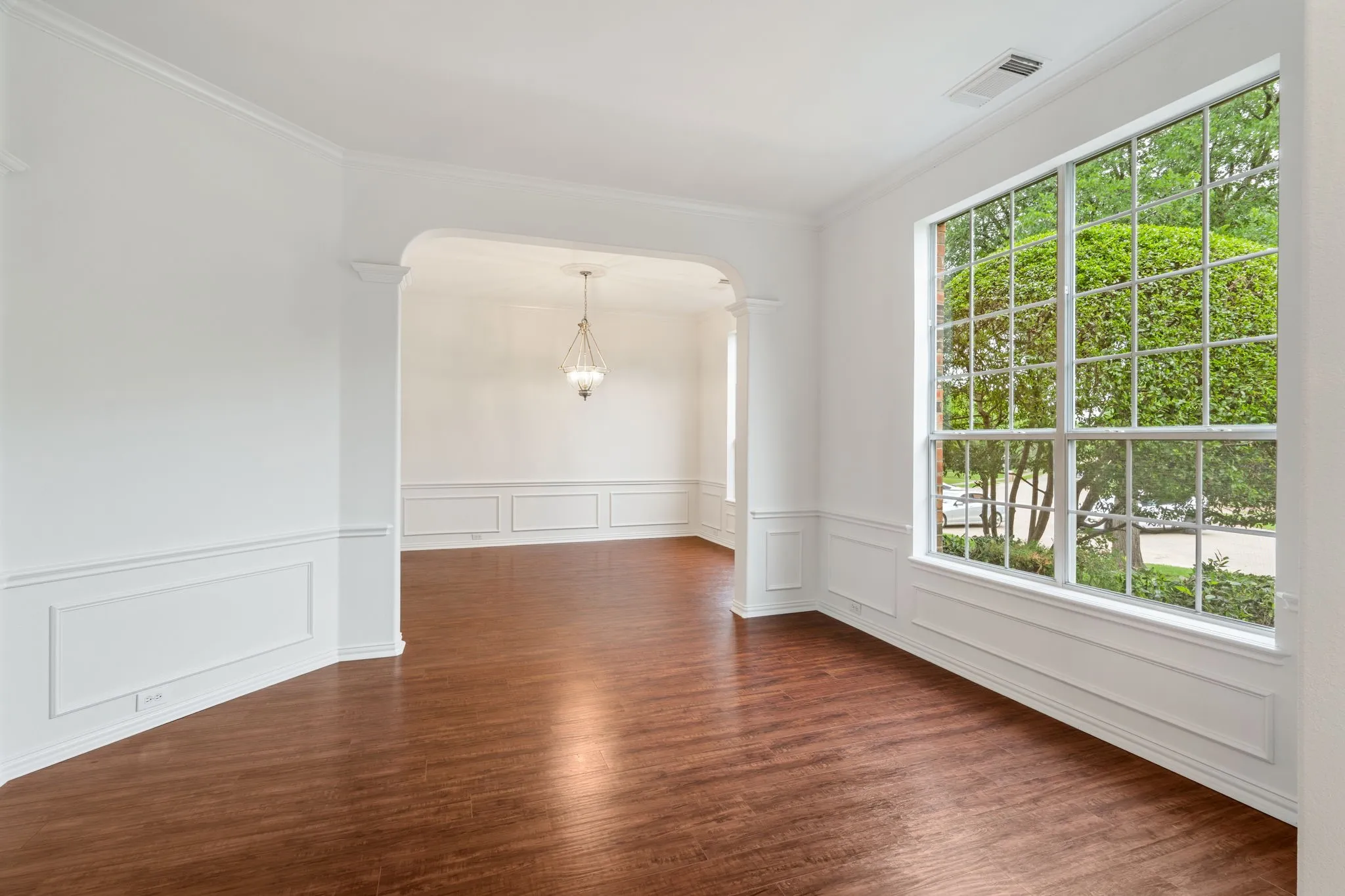 Hardwood flooring, arched doorway, wainscoting, crown molding, and large multi-pane window