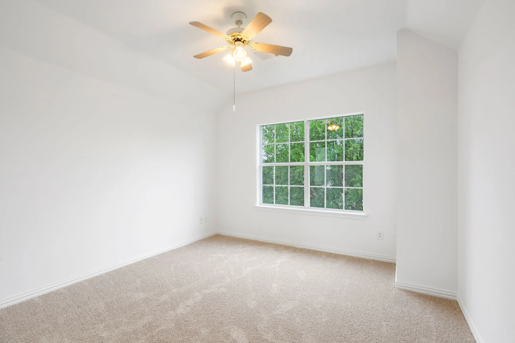 Vaulted ceiling with an attached ceiling fan and light fixture, large window, and light-toned carpeting