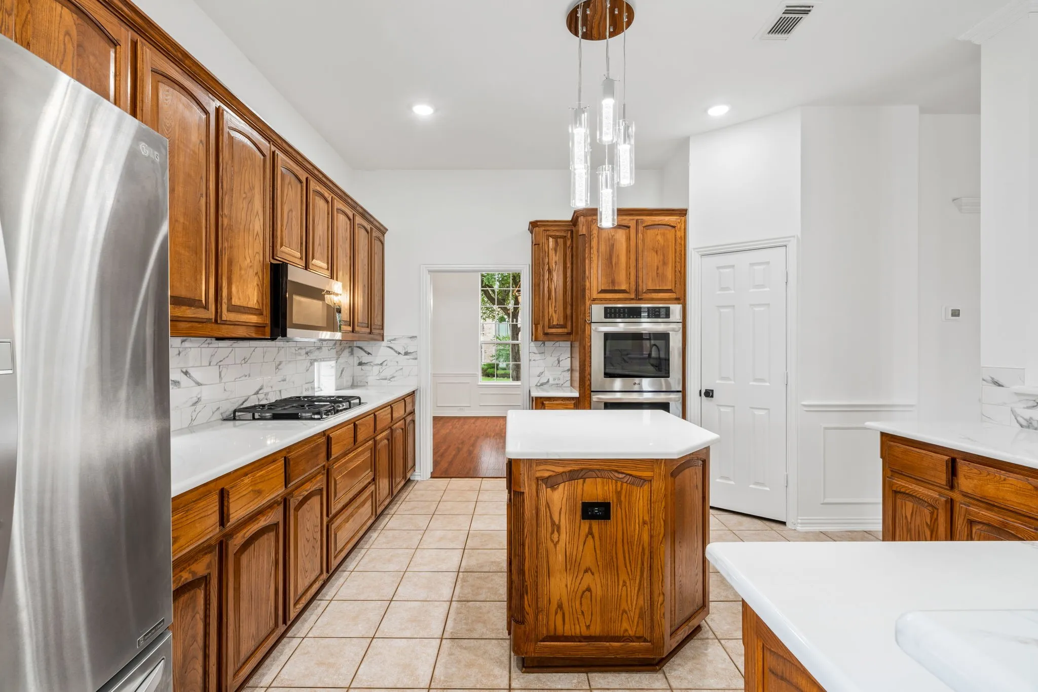 Kitchen featuring wood cabinetry, stainless steel appliances, white countertops, tile flooring, and a decorative pendant light fixture