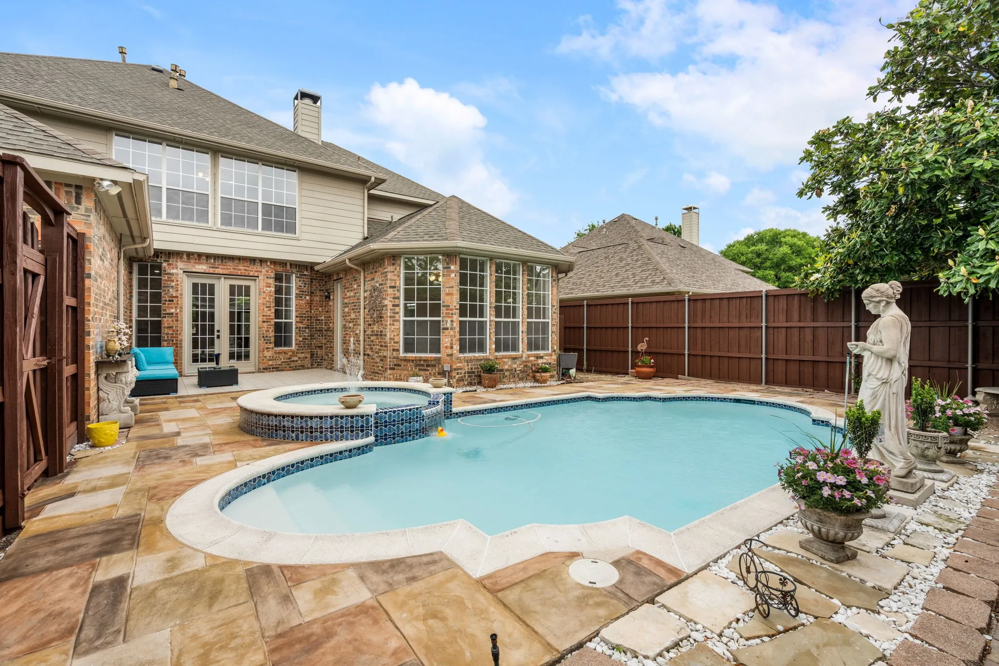 Expansive backyard featuring a custom pool with a built-in spa, brick and siding exterior, and a large patio area