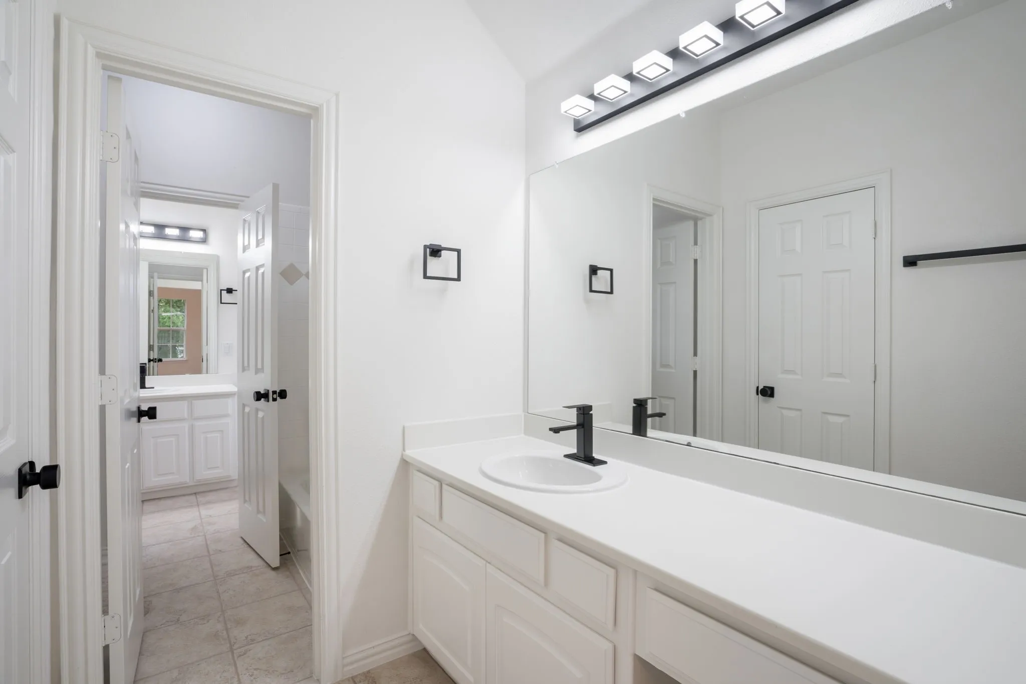 Dual vanities with white cabinetry and countertops, integrated rectangular sinks, and matte black single-handle faucets