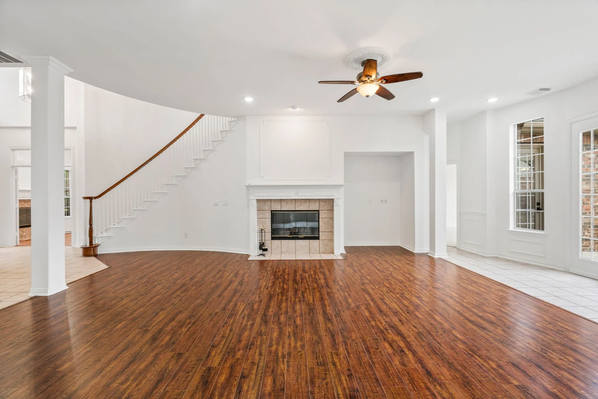 Spacious living area featuring wood-finish flooring, a fireplace with a tile surround, and a ceiling fan