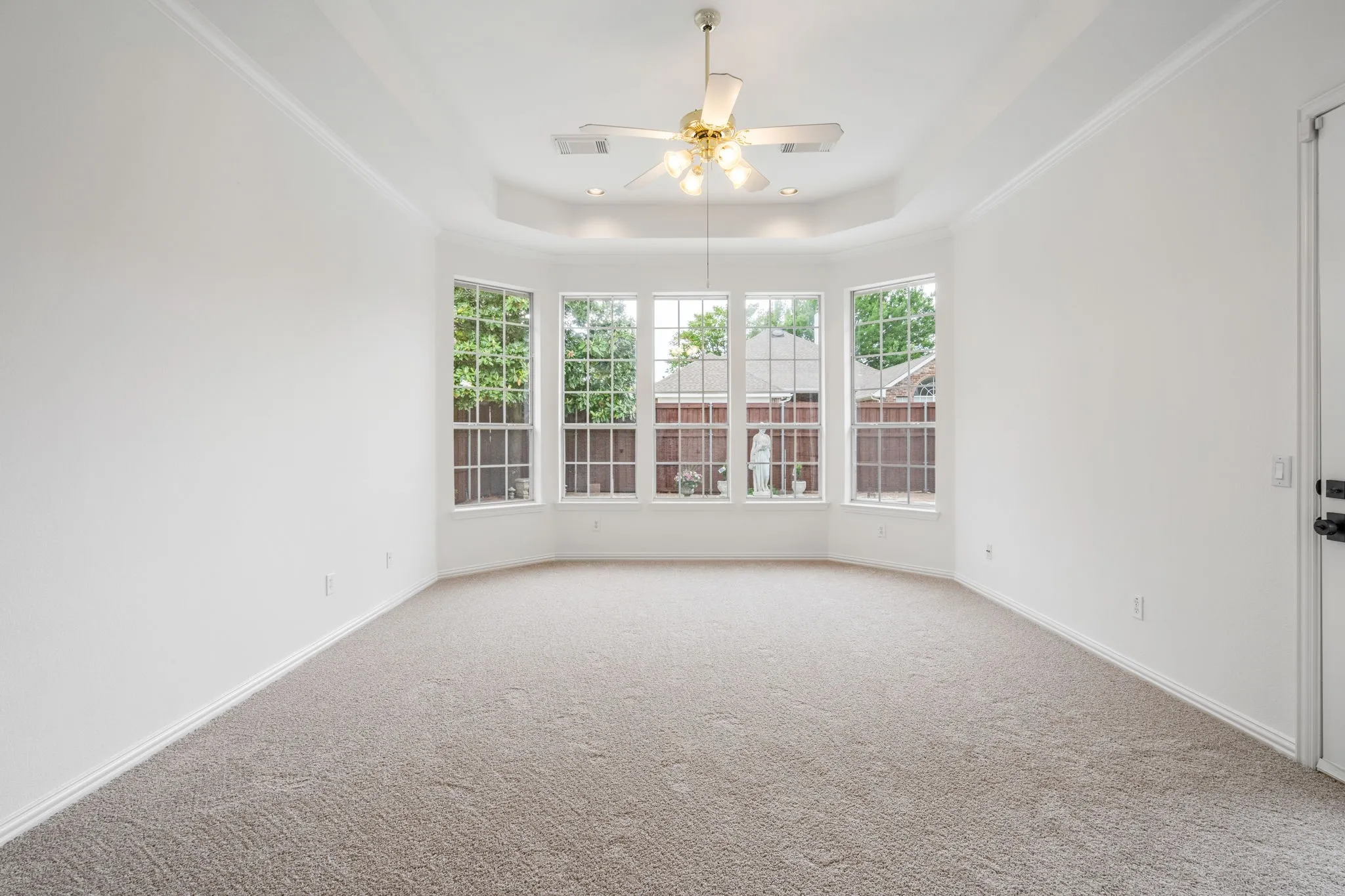 Recessed bay window, neutral carpeting, tray ceiling, ceiling fan, and crown molding