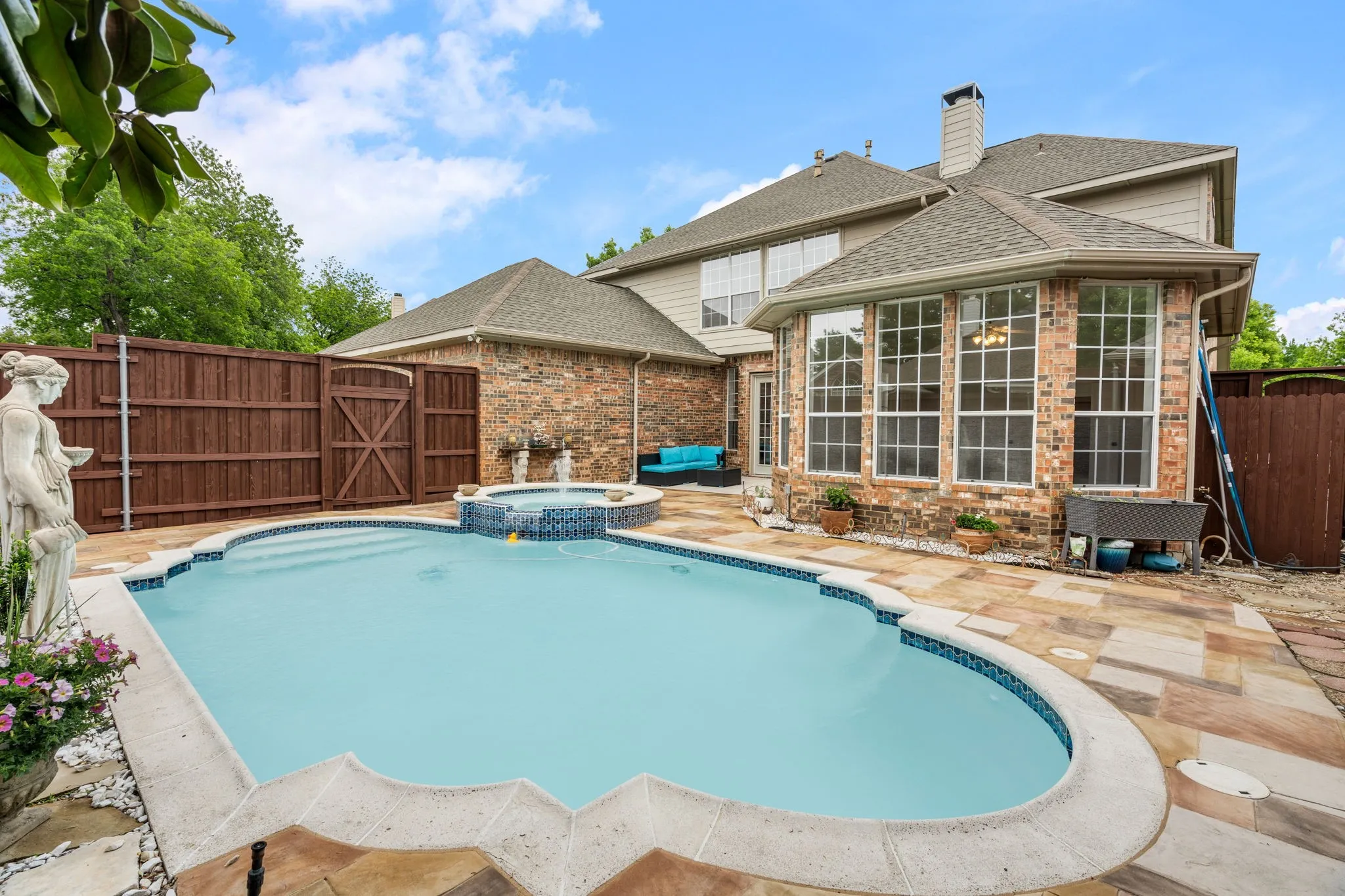 Brick exterior with multiple windows, an in-ground swimming pool, and an integrated spa