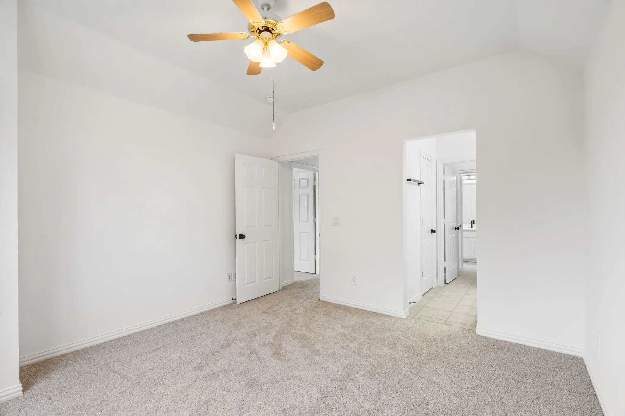Vaulted ceiling with an attached ceiling fan, neutral wall finishes, carpeted flooring, and a white paneled door