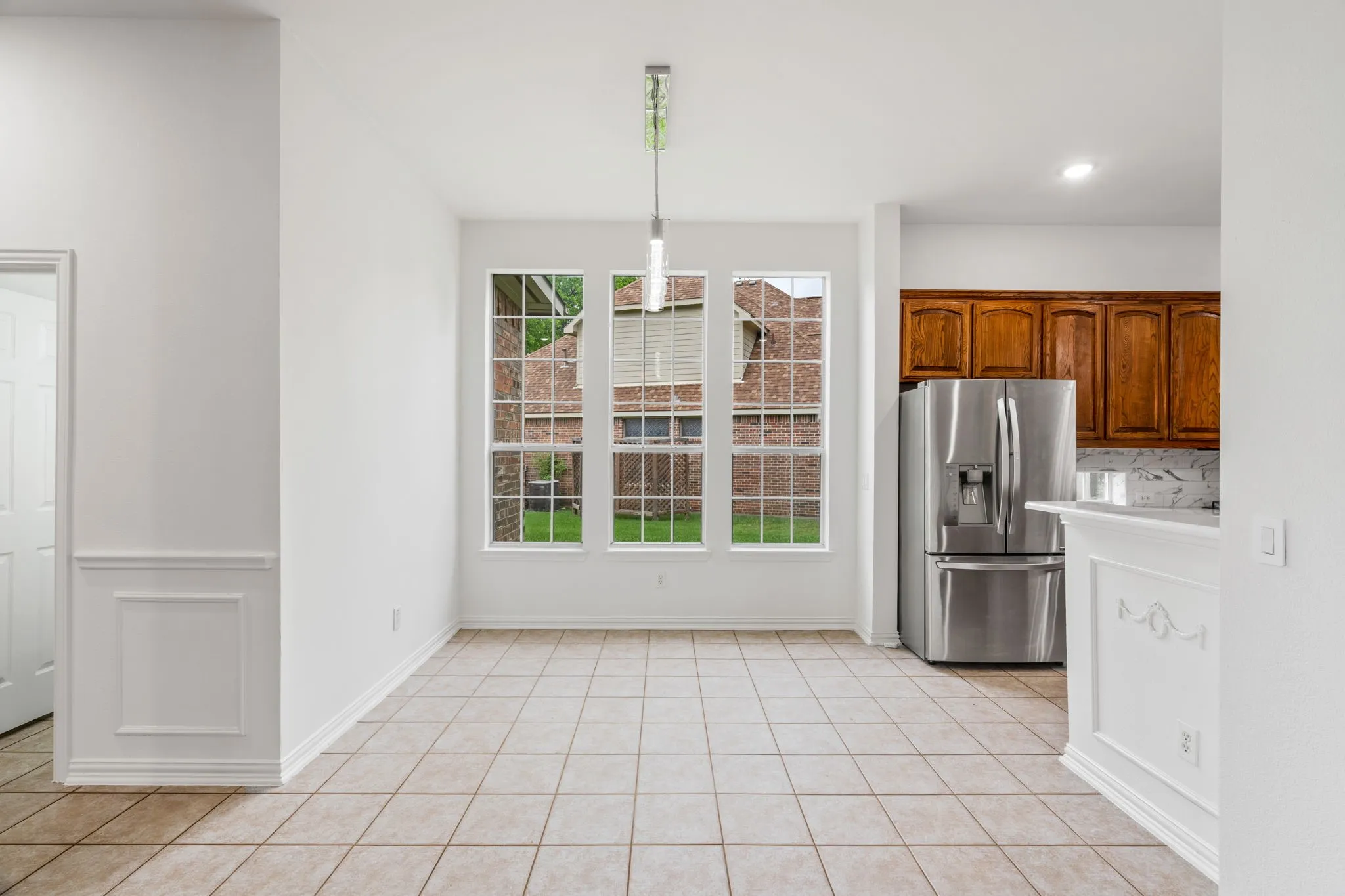 Tile flooring, three large windows, recessed lighting, wood cabinetry, and a stainless steel refrigerator