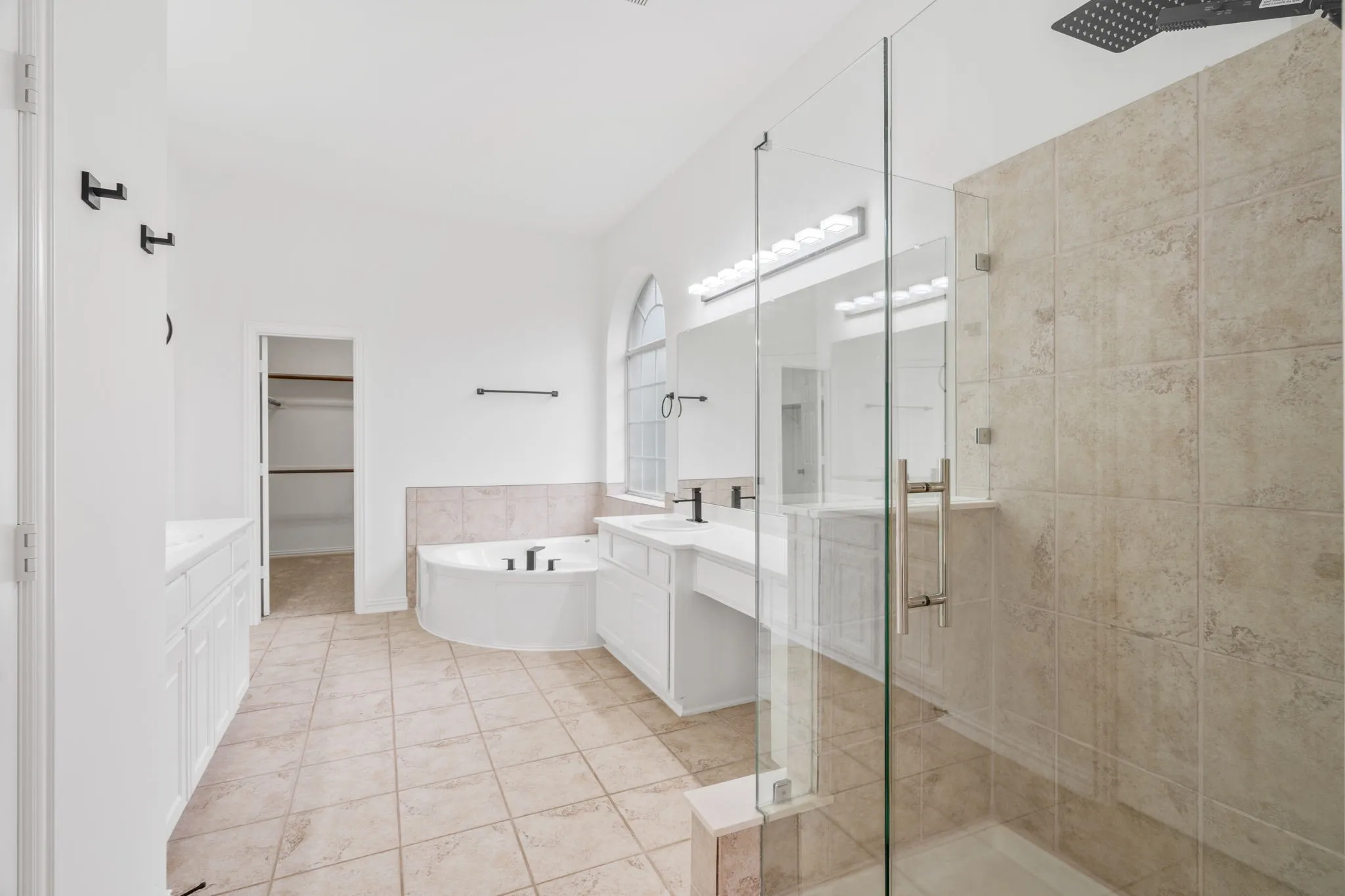 Spacious bathroom featuring a built-in soaking tub, glass-enclosed shower, dual vanity with undermount sinks, and tile flooring