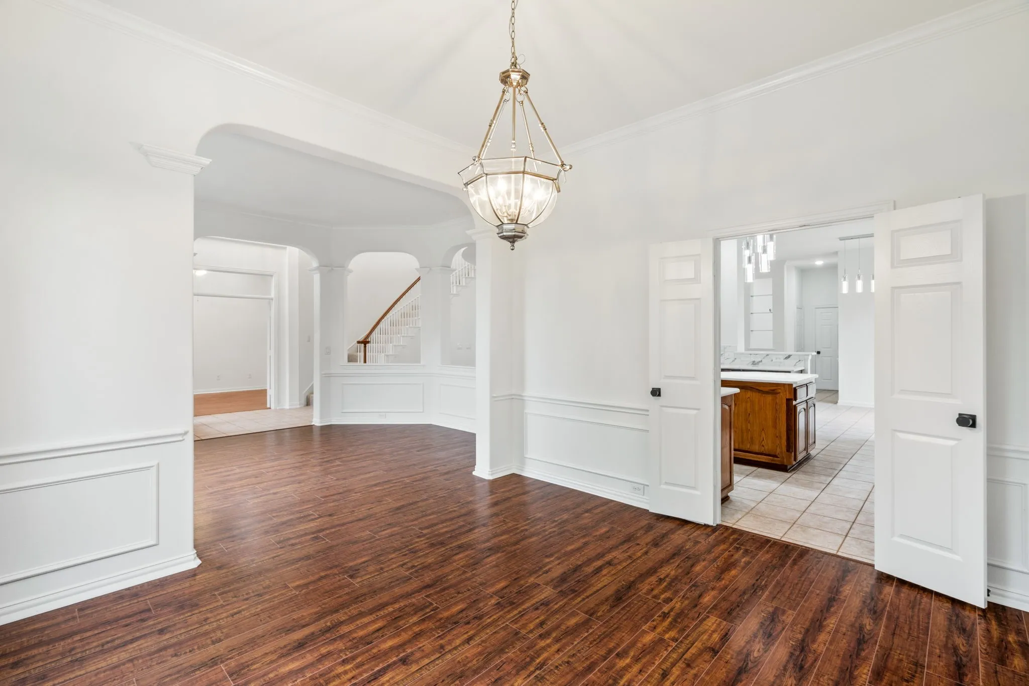 Hardwood-style flooring, wainscoting, arched entryway, and a hanging chandelier