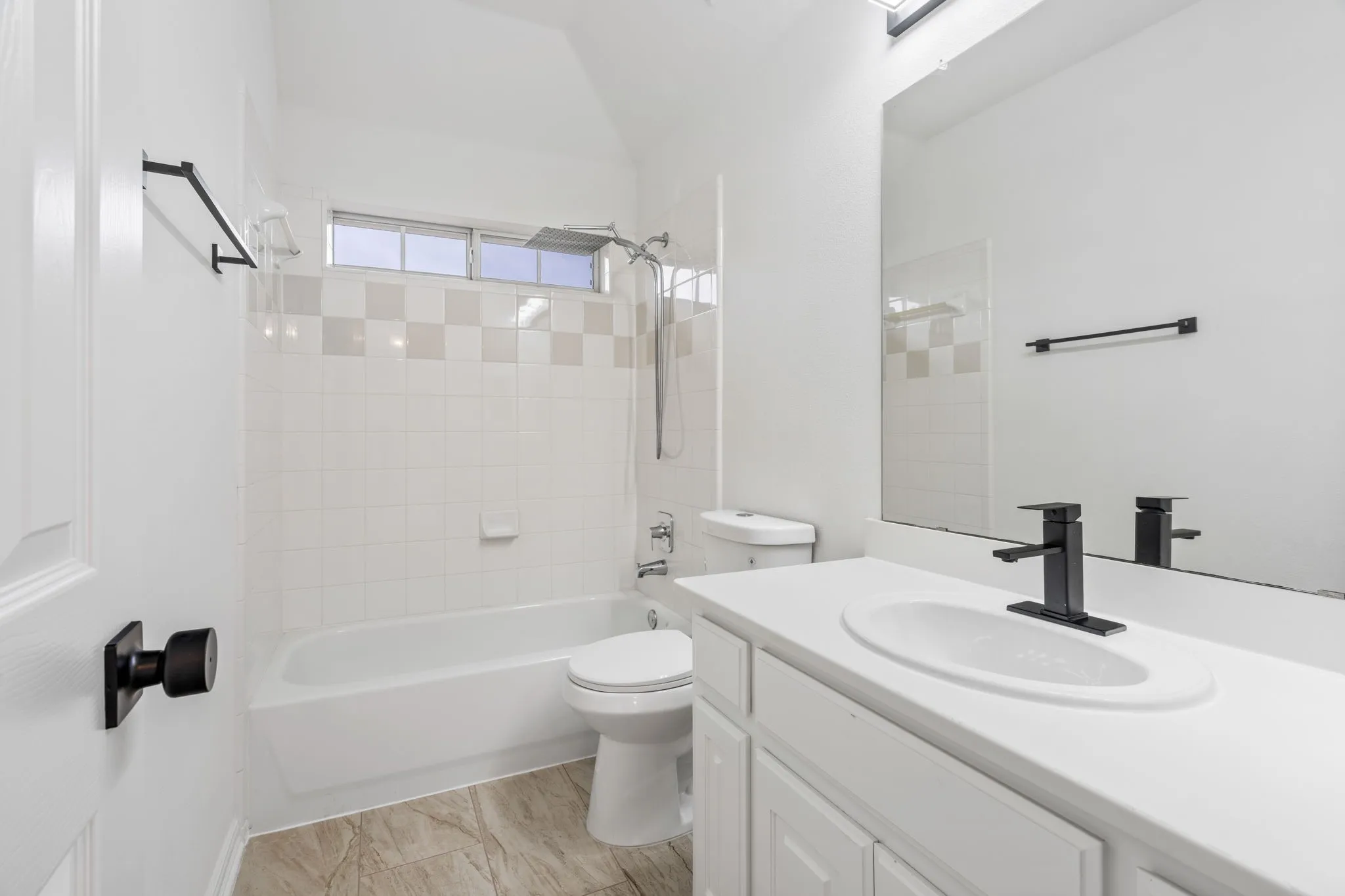 White subway tile shower surround with a decorative accent band, tub, vanity with a white countertop, and a black matte faucet