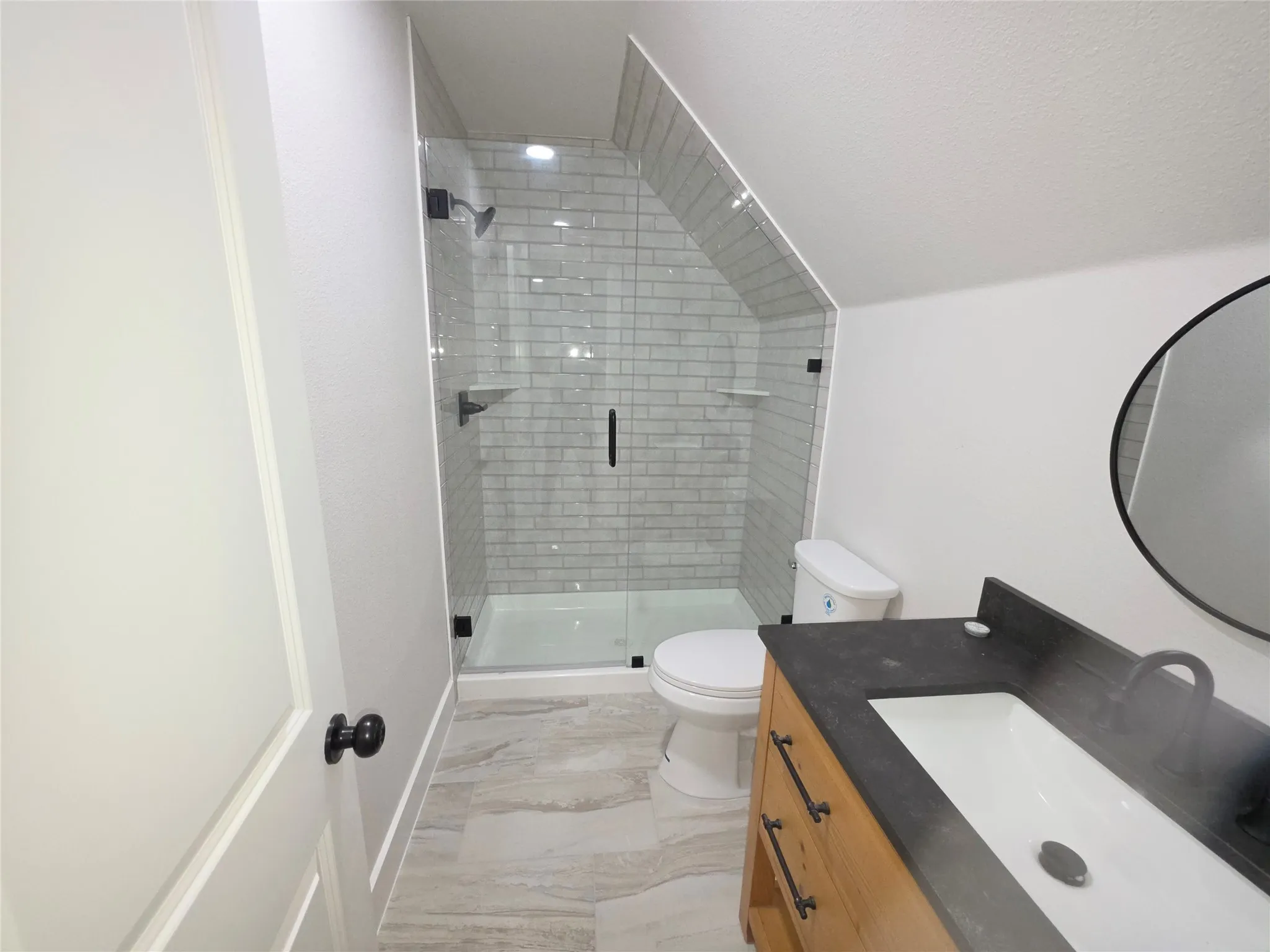 Walk-in shower featuring subway tile surround and a frameless glass enclosure, paired with a vanity boasting a dark countertop and matte black hardware
