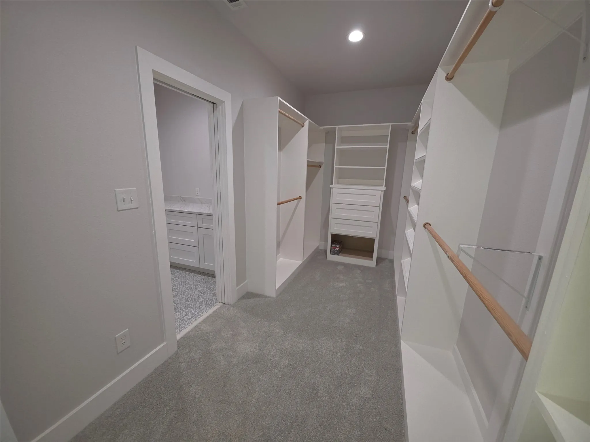Walk-in closet featuring custom white shelving, integrated wooden clothing rods, and a built-in drawer unit