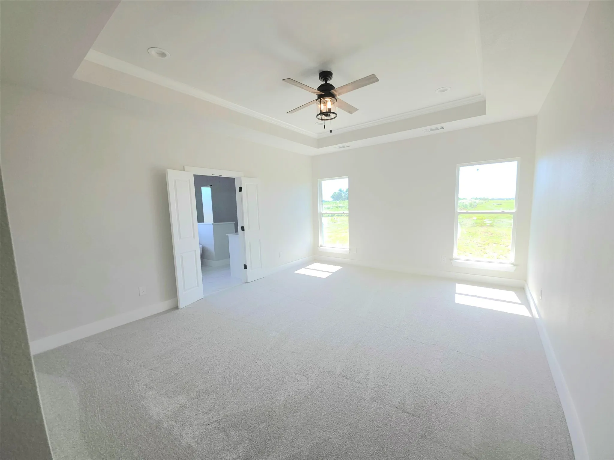 Spacious room featuring a tray ceiling, neutral wall-to-wall carpeting, recessed lighting, a multi-blade ceiling fan with integrated light fixture, and double door entry