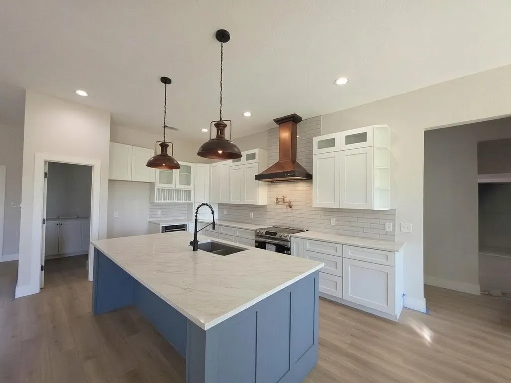 Kitchen featuring a central island with a stone countertop, white cabinetry with glass-front accents, a tiled backsplash, a metal range hood, and wood-finish flooring