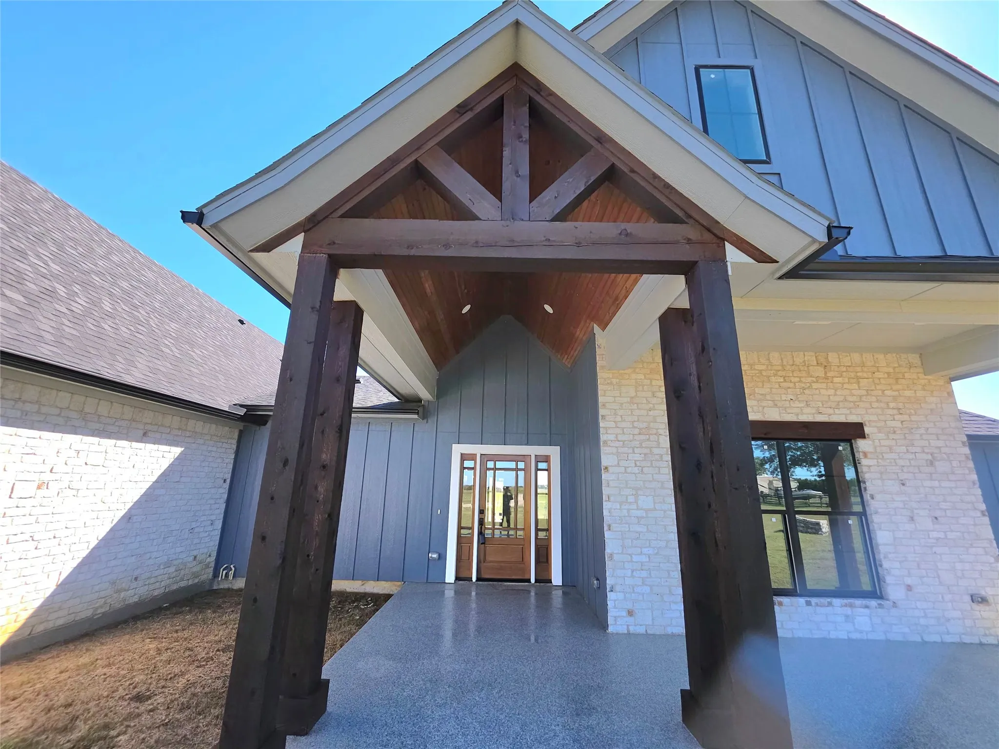 Exterior entry featuring stone and vertical board-and-batten siding, timber-frame gable roof with wood-paneled ceiling, and a multi-lite wood front door