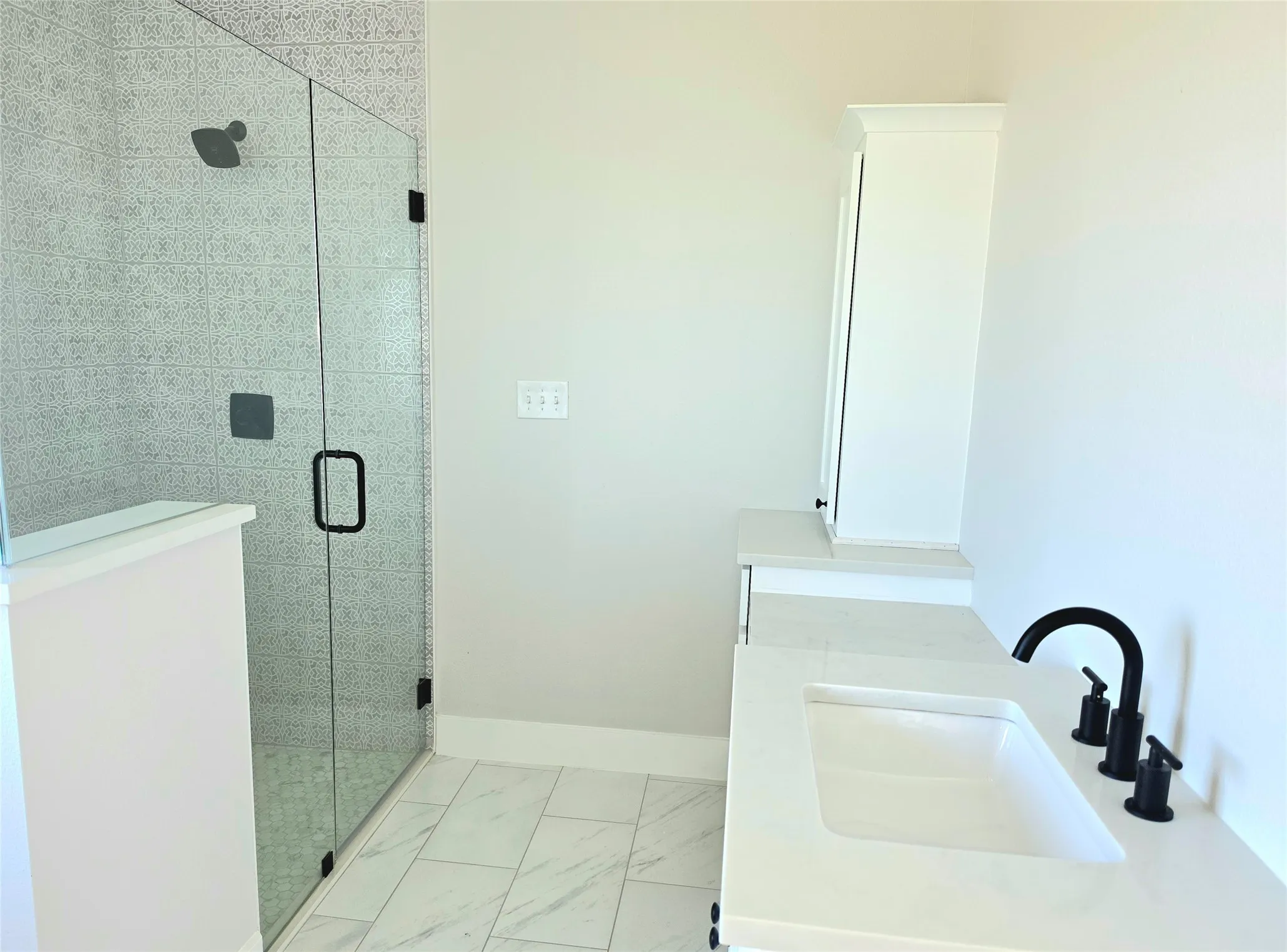 Bathroom featuring a glass-enclosed shower with matte black fixtures, stone-finish vanity countertop with an undermount sink, and large-format tile flooring