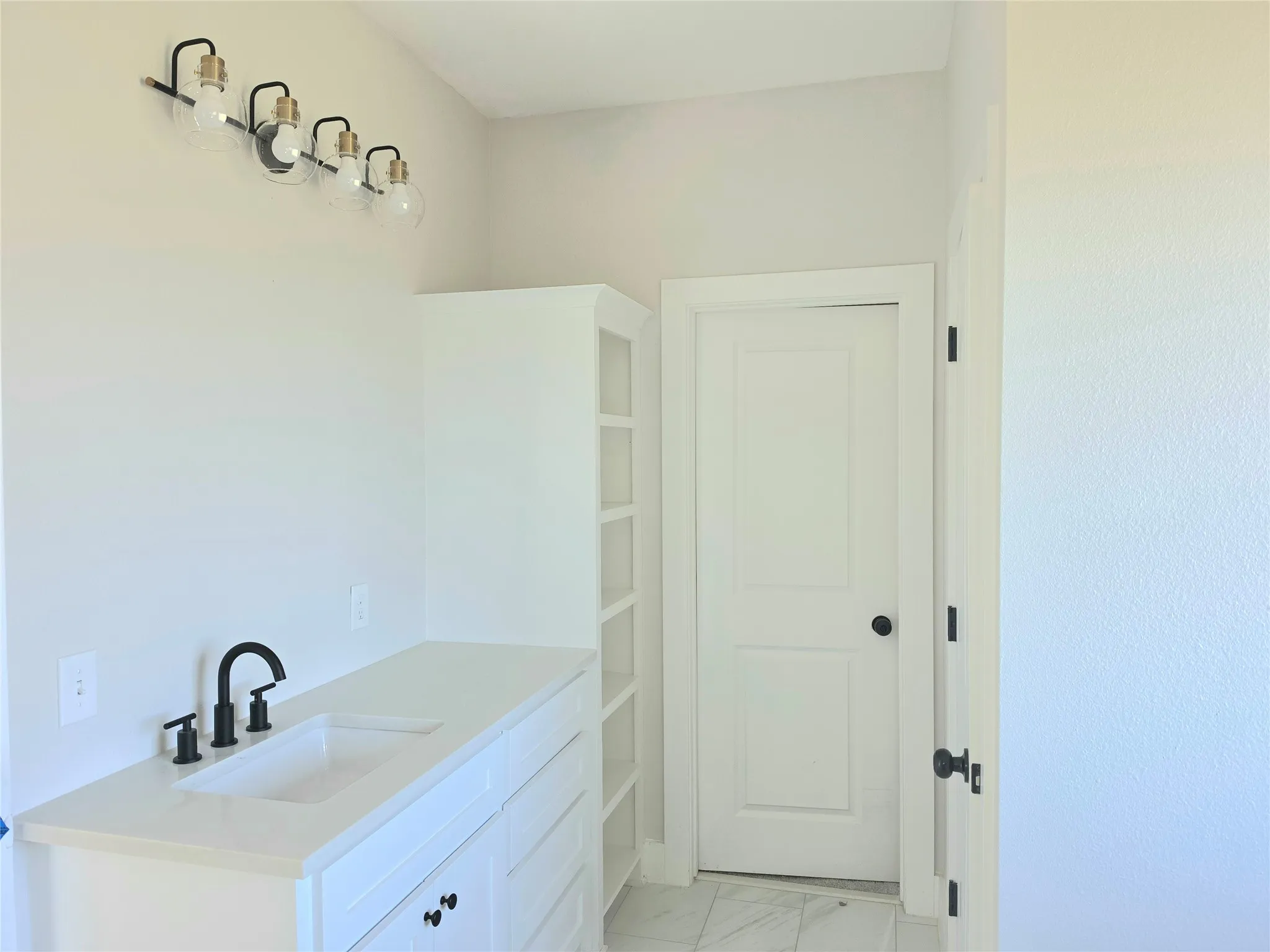 White vanity with a rectangular undermount sink, quartz countertop, matte black widespread faucet, integrated shelving, and a four-light fixture with globe bulbs