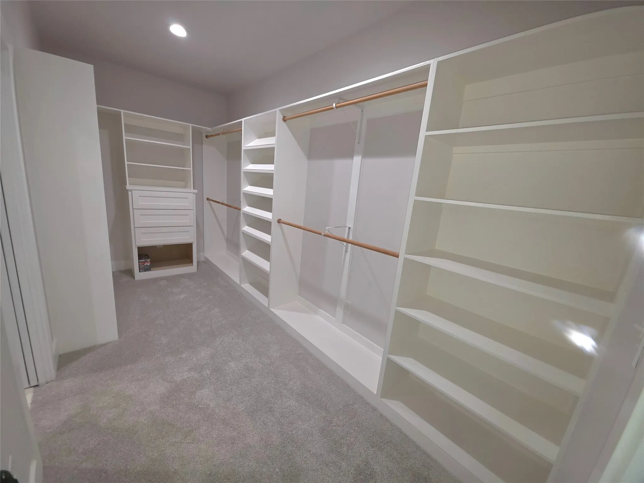 Custom walk-in closet featuring extensive white built-in shelving, integrated dresser drawers, wooden hanging rods, and neutral carpeting