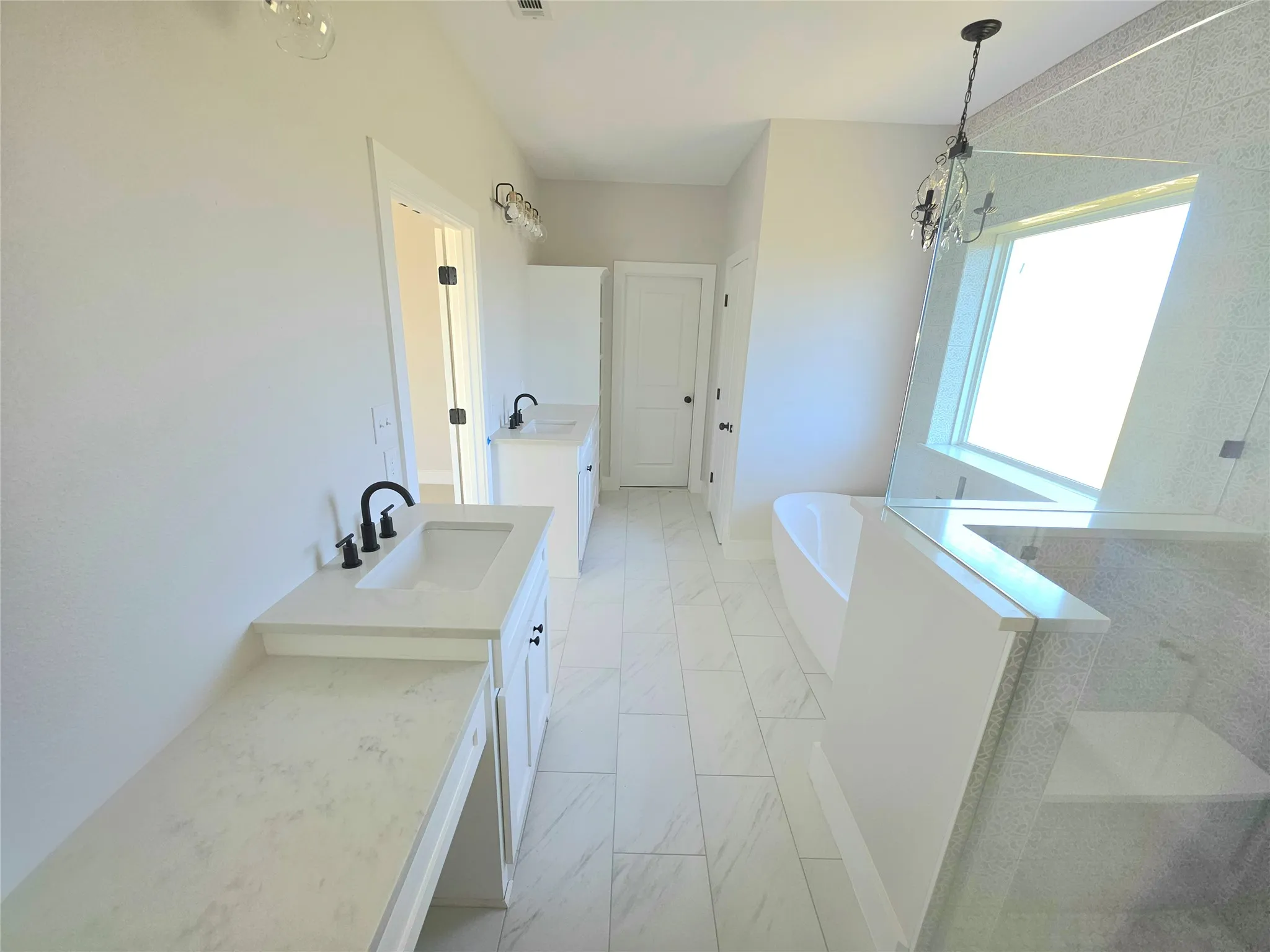 Bathroom featuring white cabinetry with light-toned stone-patterned countertops, dual undermount sinks with matte black fixtures, a freestanding soaking tub, and a glass-enclosed shower with tiled walls and a built-in bench