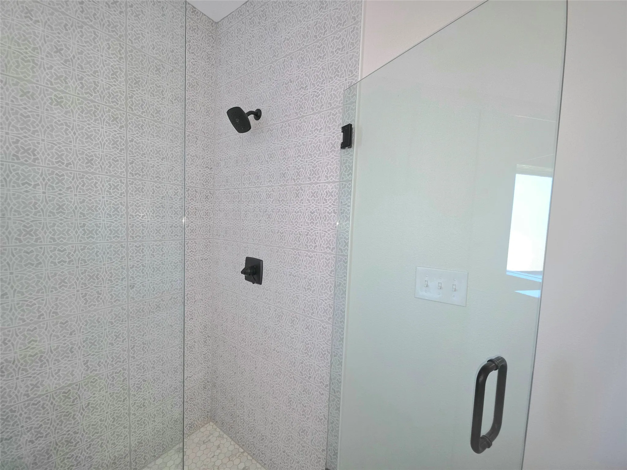 Shower stall featuring patterned tile surround, pebble-style flooring, glass enclosure with matte black hardware, and wall-mounted matte black shower fixture