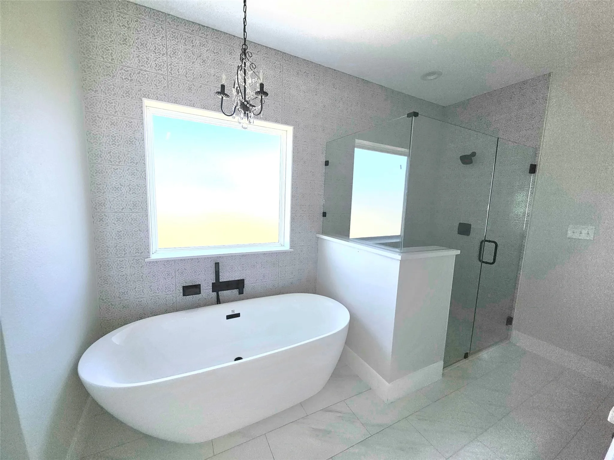 Freestanding soaking tub with wall-mounted matte black faucet, glass-enclosed shower with matte black hardware, and patterned tile wall accent