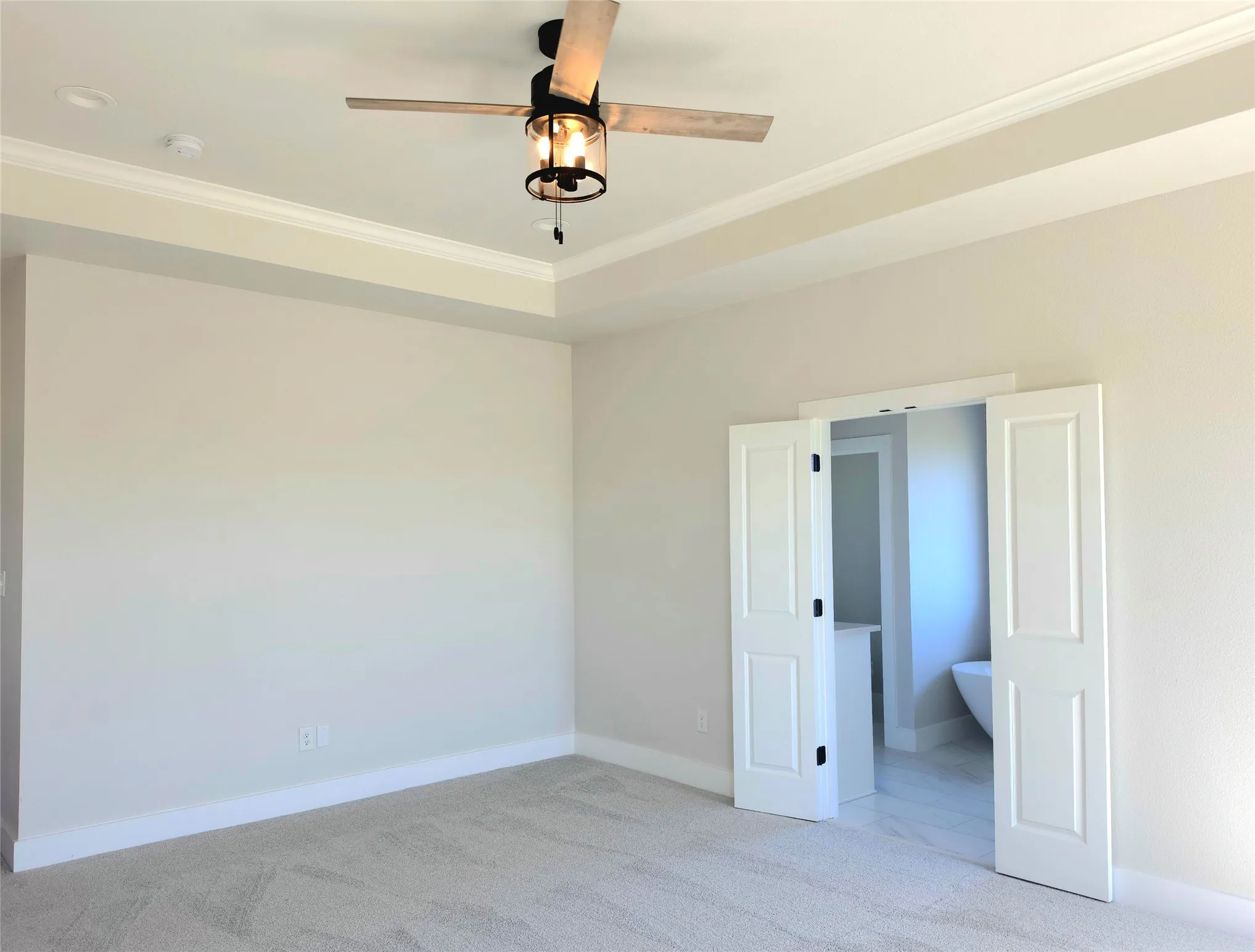 Tray ceiling with crown molding, ceiling fan with glass-enclosed lighting, and double-panel doors